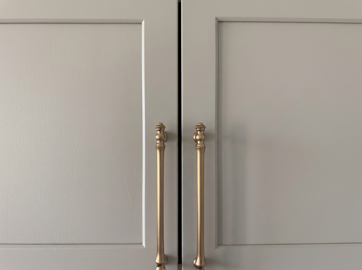 Close-up of the handles on two kitchen cabinet doors, one painted beige, the other painted gray, with a small gap between them.