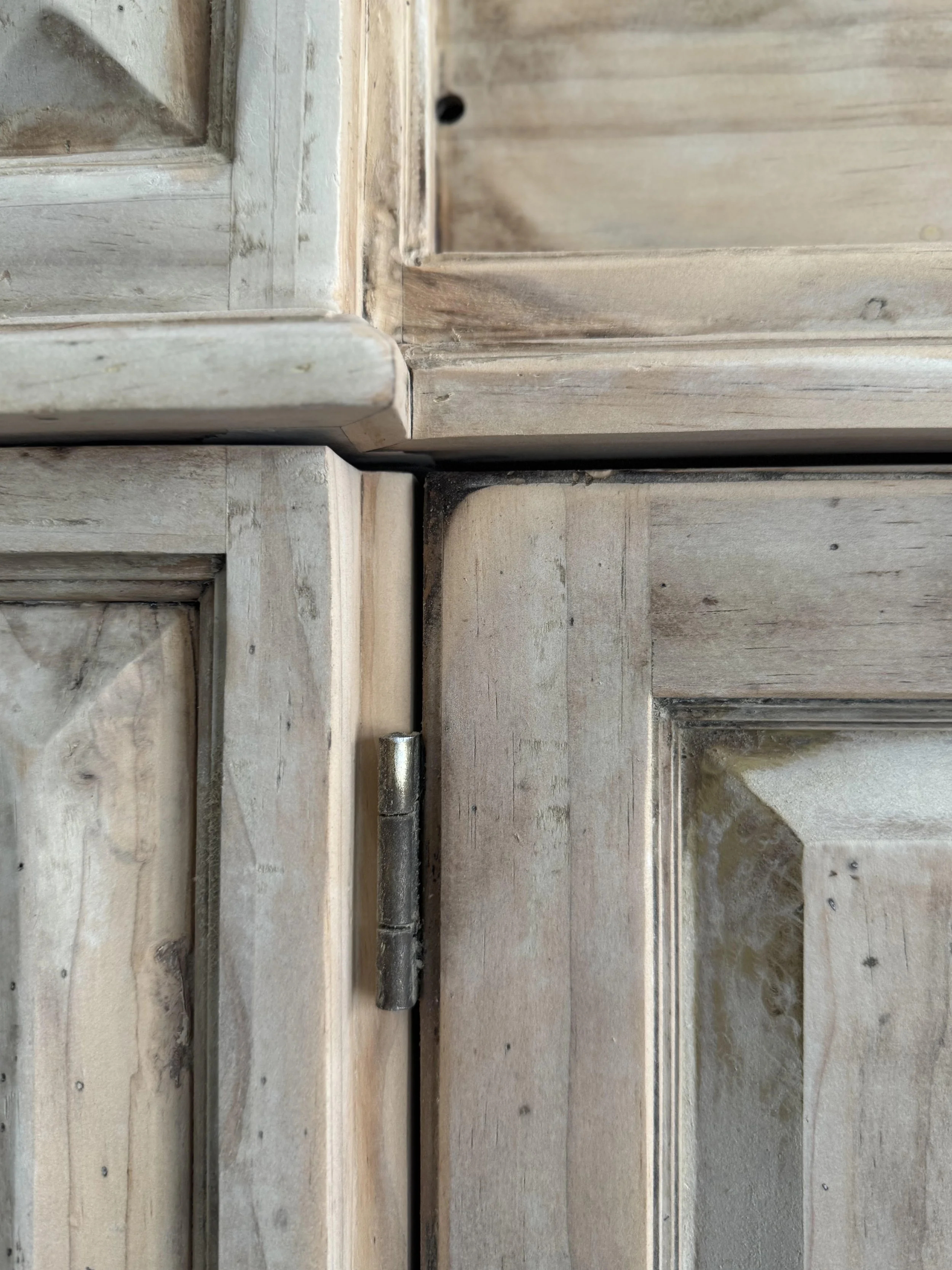 Close-up view of corner and frame of a wooden cabinet or door, showing natural wood grain and weathered surface.