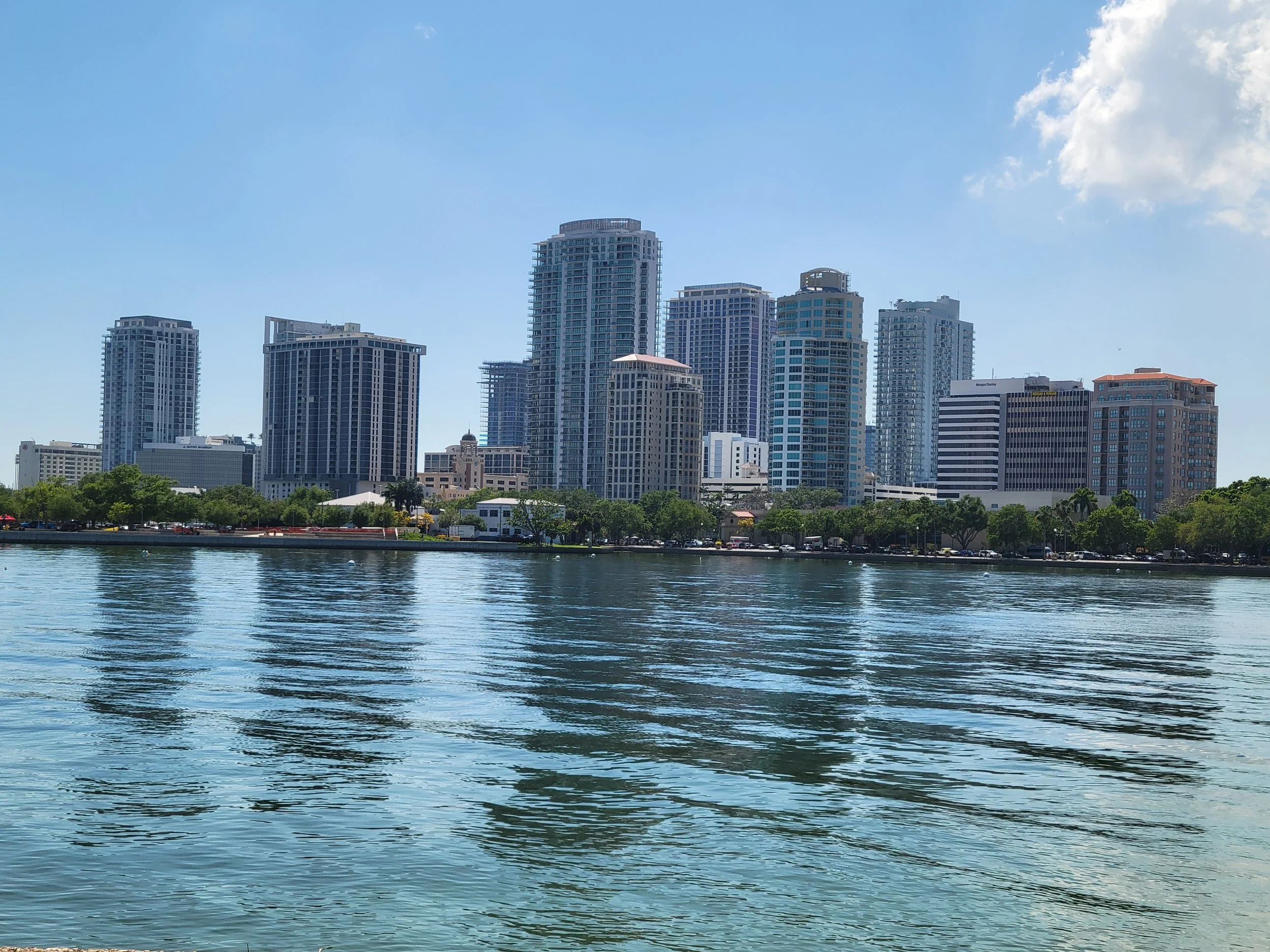 St. Petersburg Florida skyline with tall buildings seen across a body of water, under a clear blue sky.