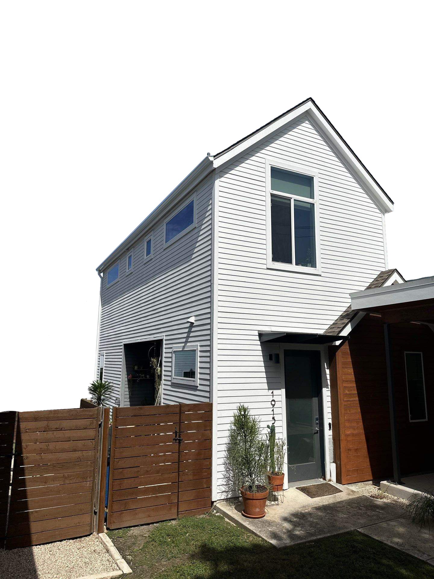 White two-story house with a wooden fence, potted plants at the front door, and a black front door beneath a small awning.
