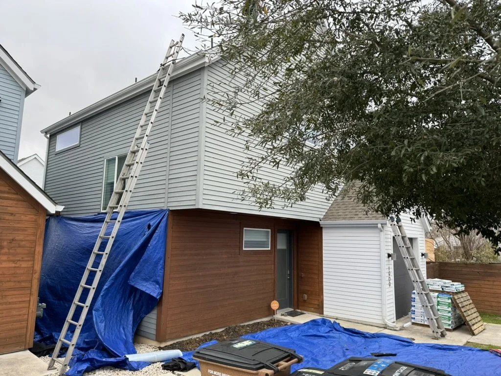 Construction or renovation of a house with ladders, blue tarps, and building materials present in the yard during daytime.