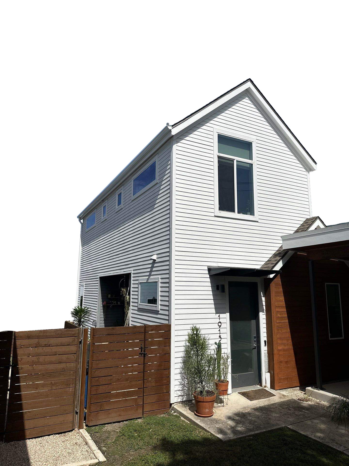 White modern two-story house with a wooden fence, potted plants near the front door, and large windows, under a partly cloudy sky.