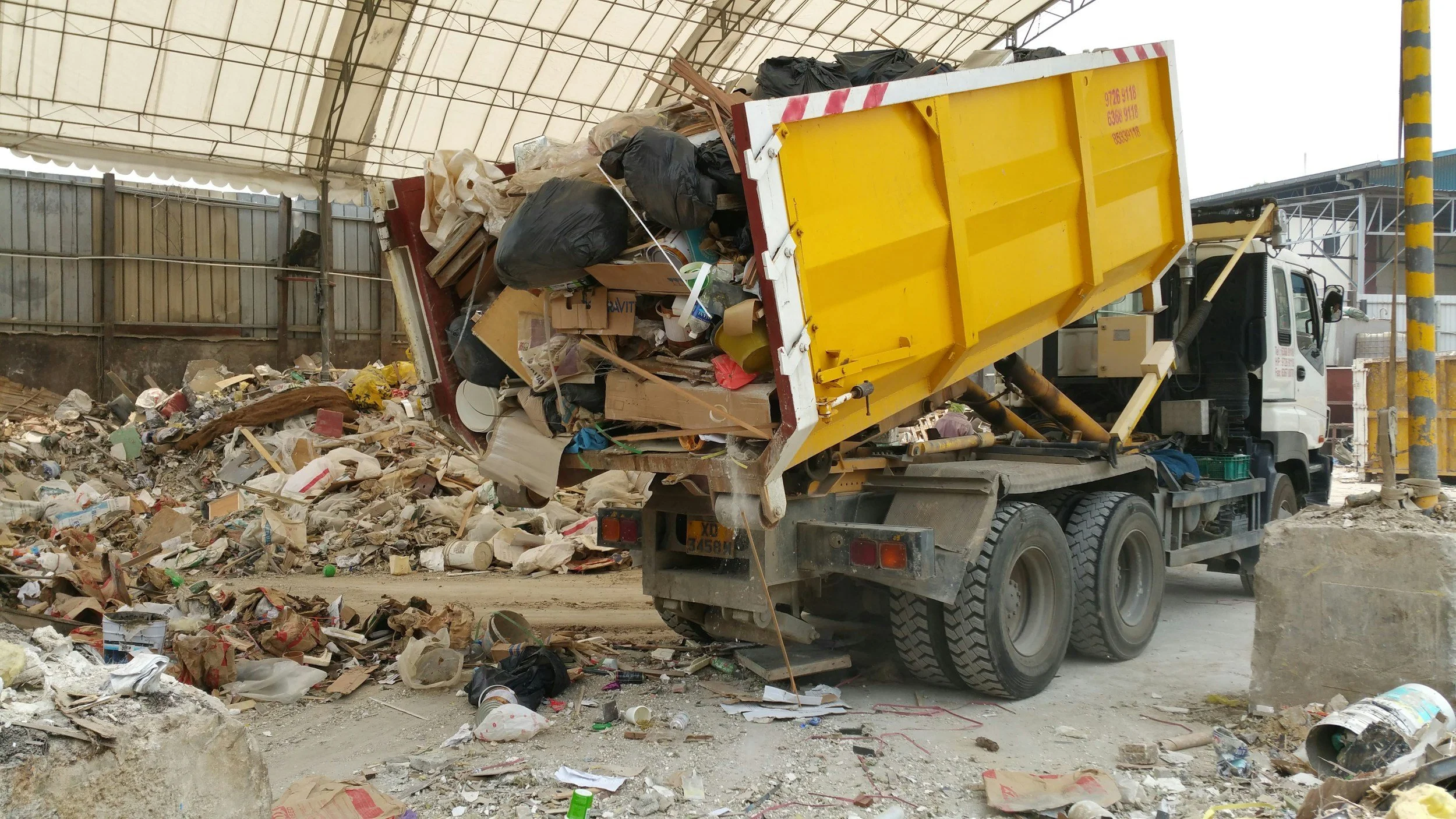 A yellow dump truck dumping trash and debris into a large pile in an industrial or construction area.