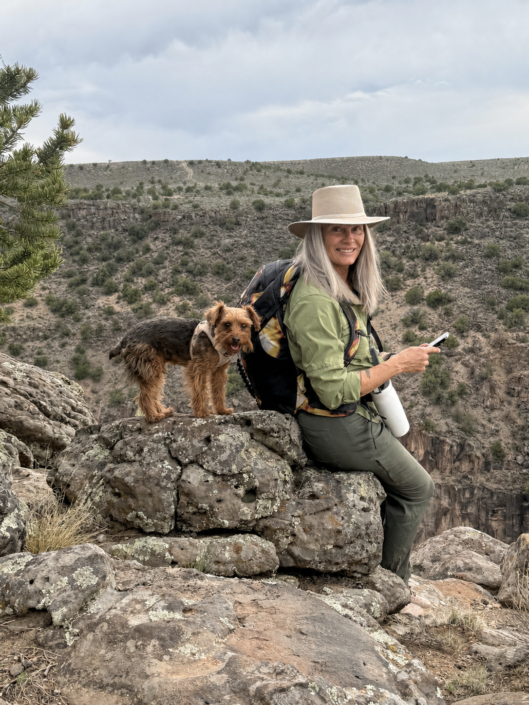 Luna sitting on rocks with her small dog in a scenic canyon.