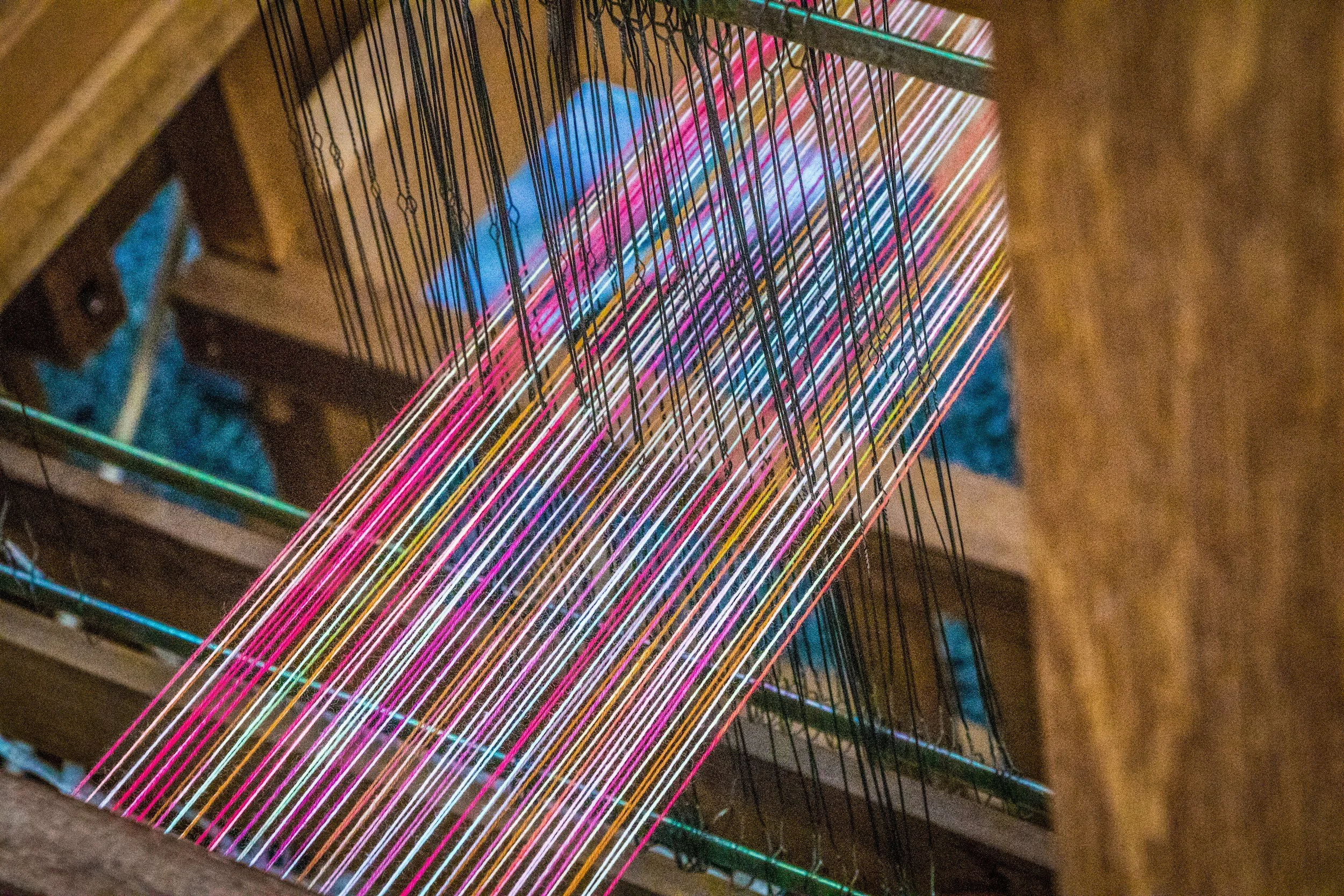 A loom with multicolored threads woven through its frame, creating a vibrant pattern of pink, white, yellow, and other colors.