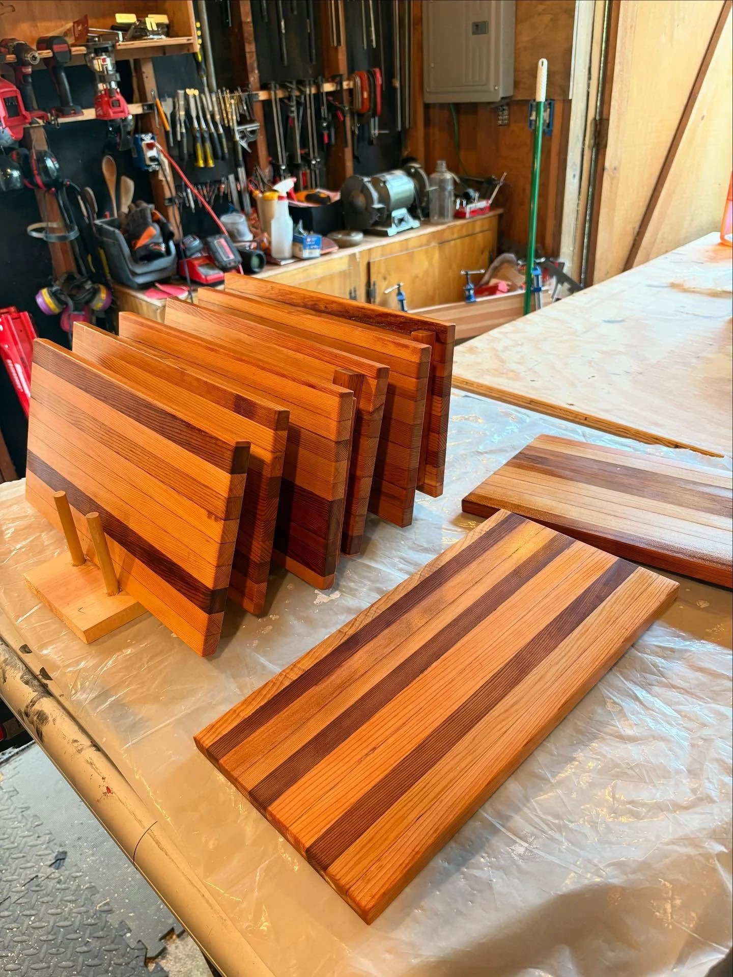 Several wooden boards with striped patterns are arranged on a work table in a woodworking shop, with tools and equipment visible in the background.