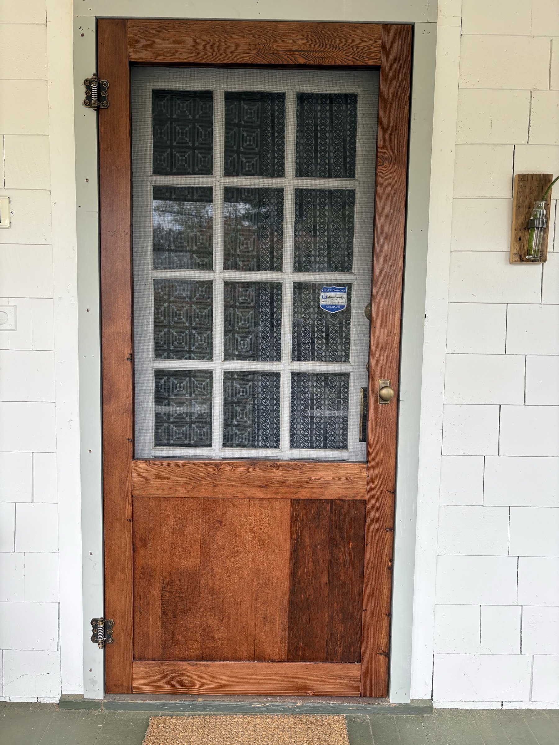 A divided-light screen door with textured glass and brass hardware.