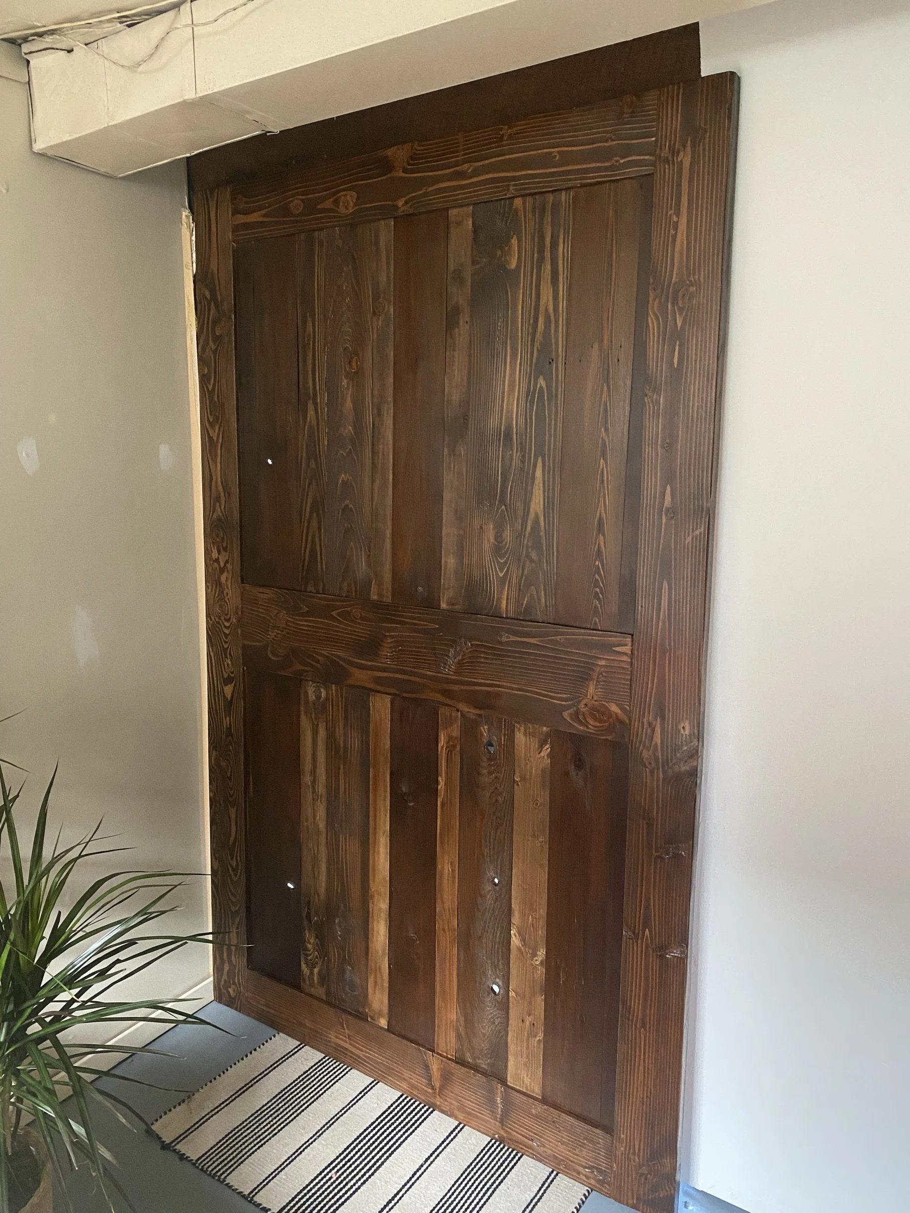 A dark-stained sliding barn door installed beside a plant and rug.