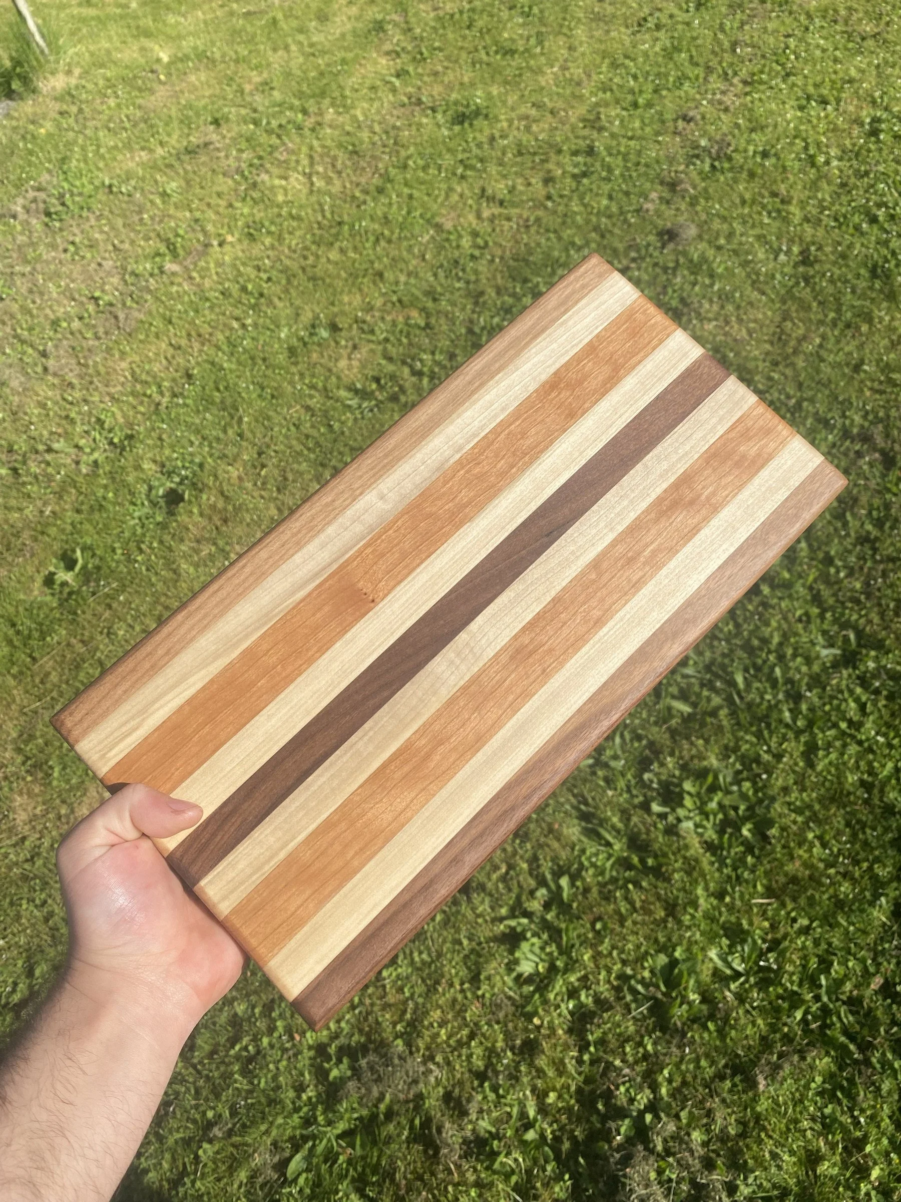 A striped cutting board held up against the grass.