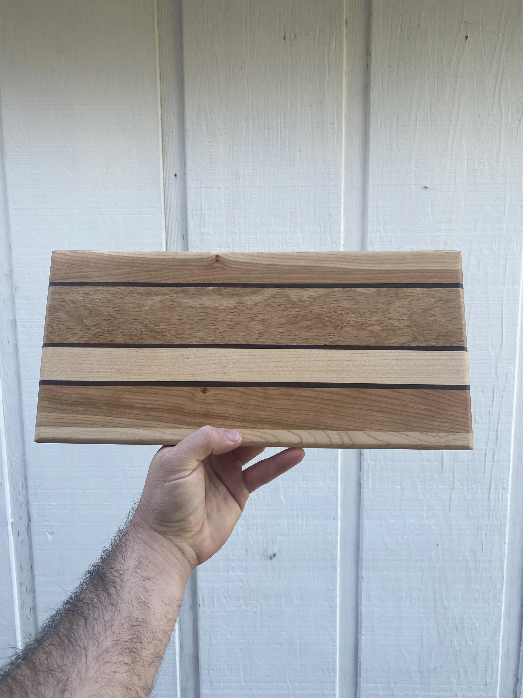 A maple and walnut cutting board against a white wall.