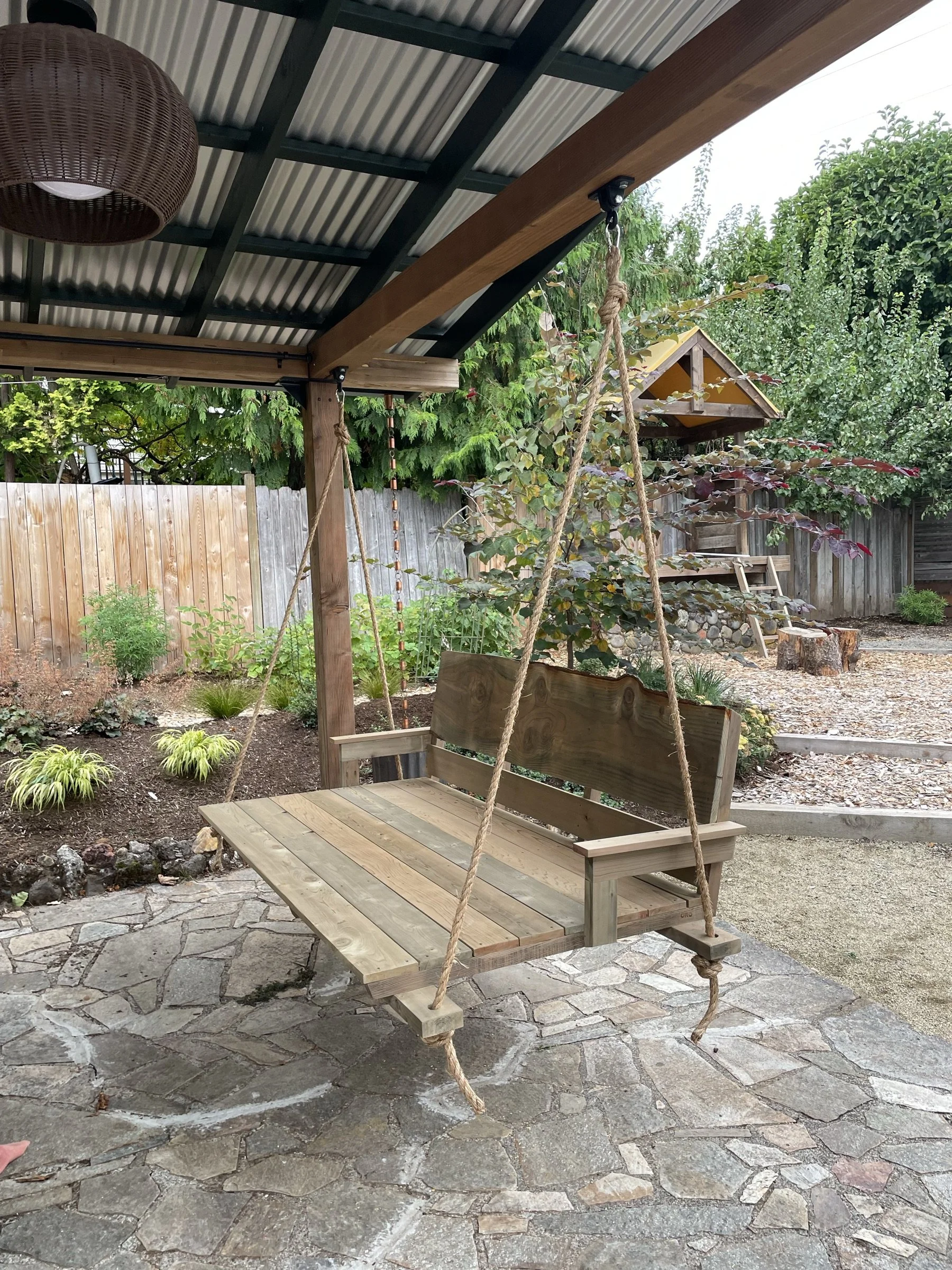 Cedar daybed-style swing hanging under a garden pergola.