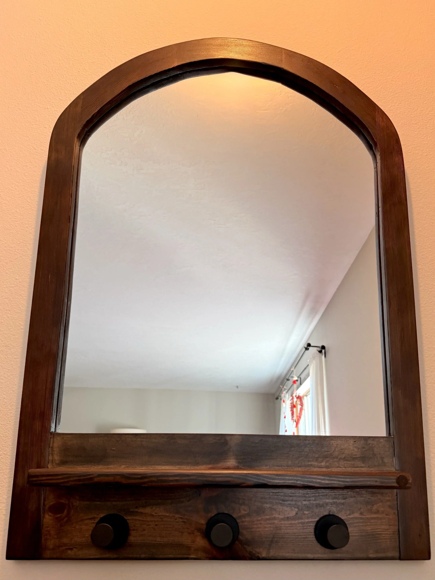Arched dark-stained mirror in a reclaimed-fir frame with a peg rail.