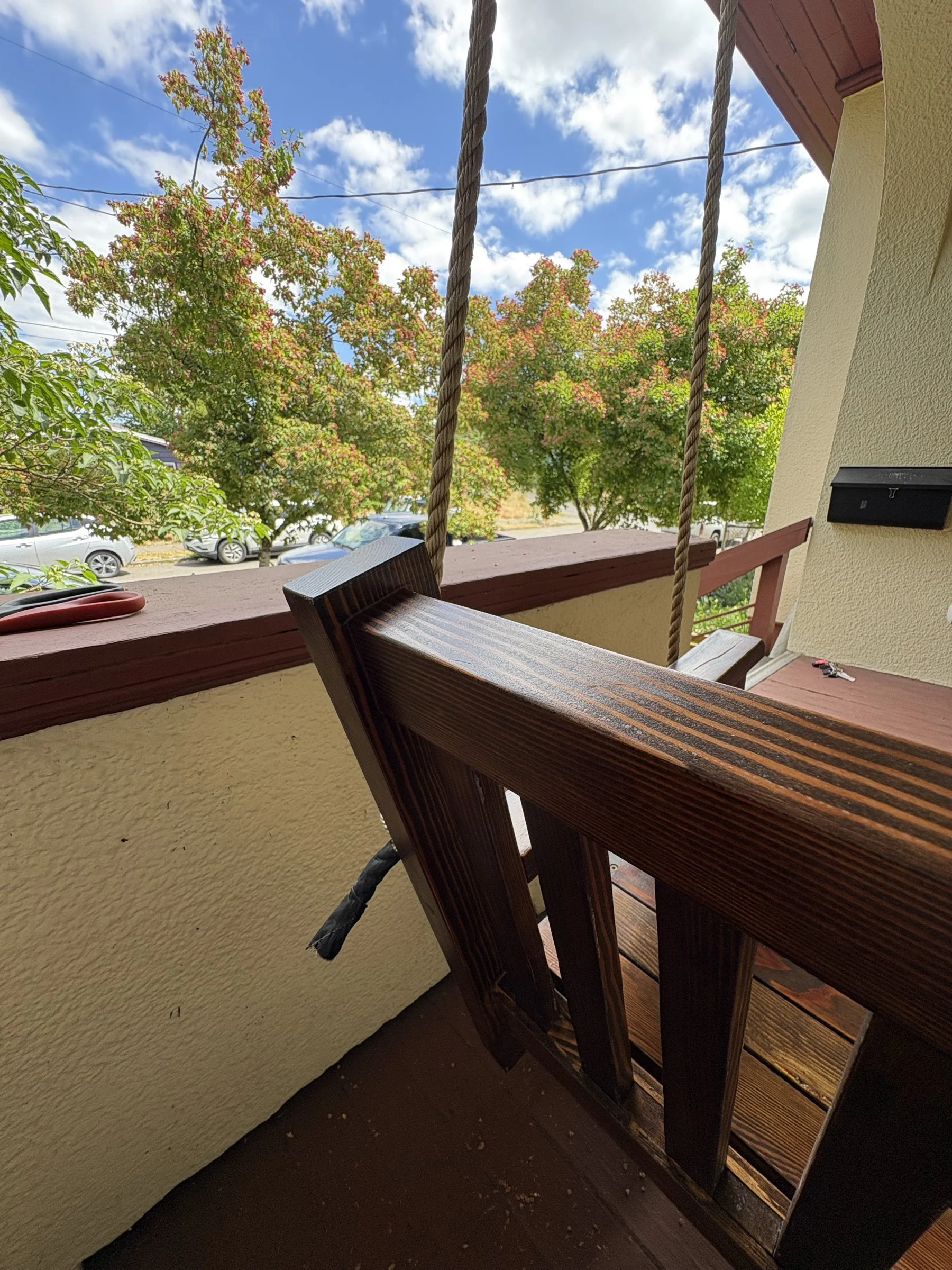 The porch swing arm and hanging rope with a neighborhood view behind.