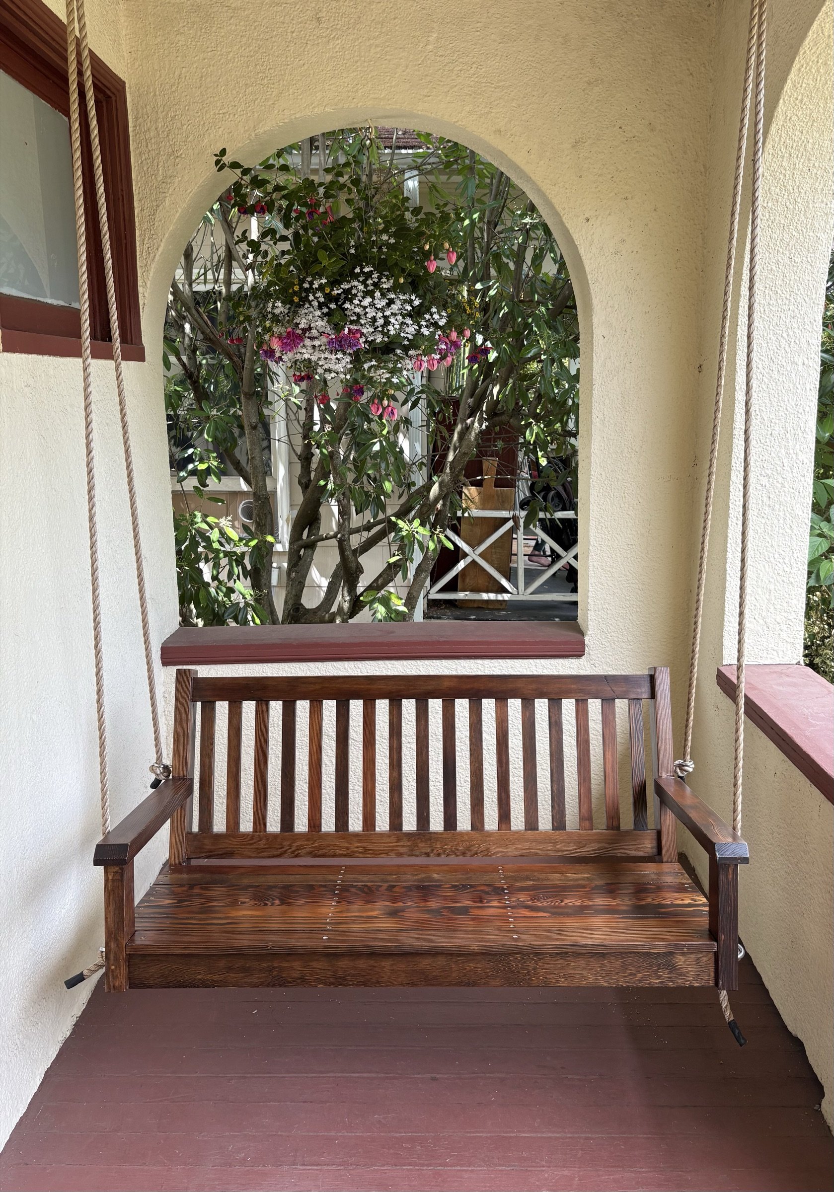 Reclaimed-fir porch swing framed by an arched porch opening, flowers behind.