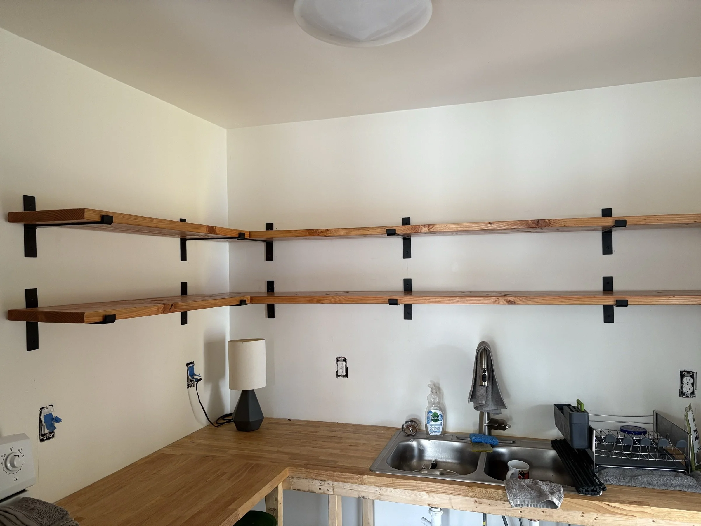 Long floating wall shelves on black brackets in a bright room.
