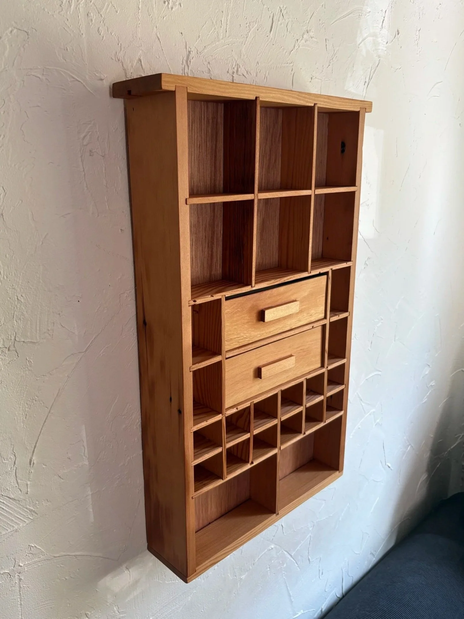 A lighter oak curio shelf with two drawers and open compartments, mounted on a plaster wall.