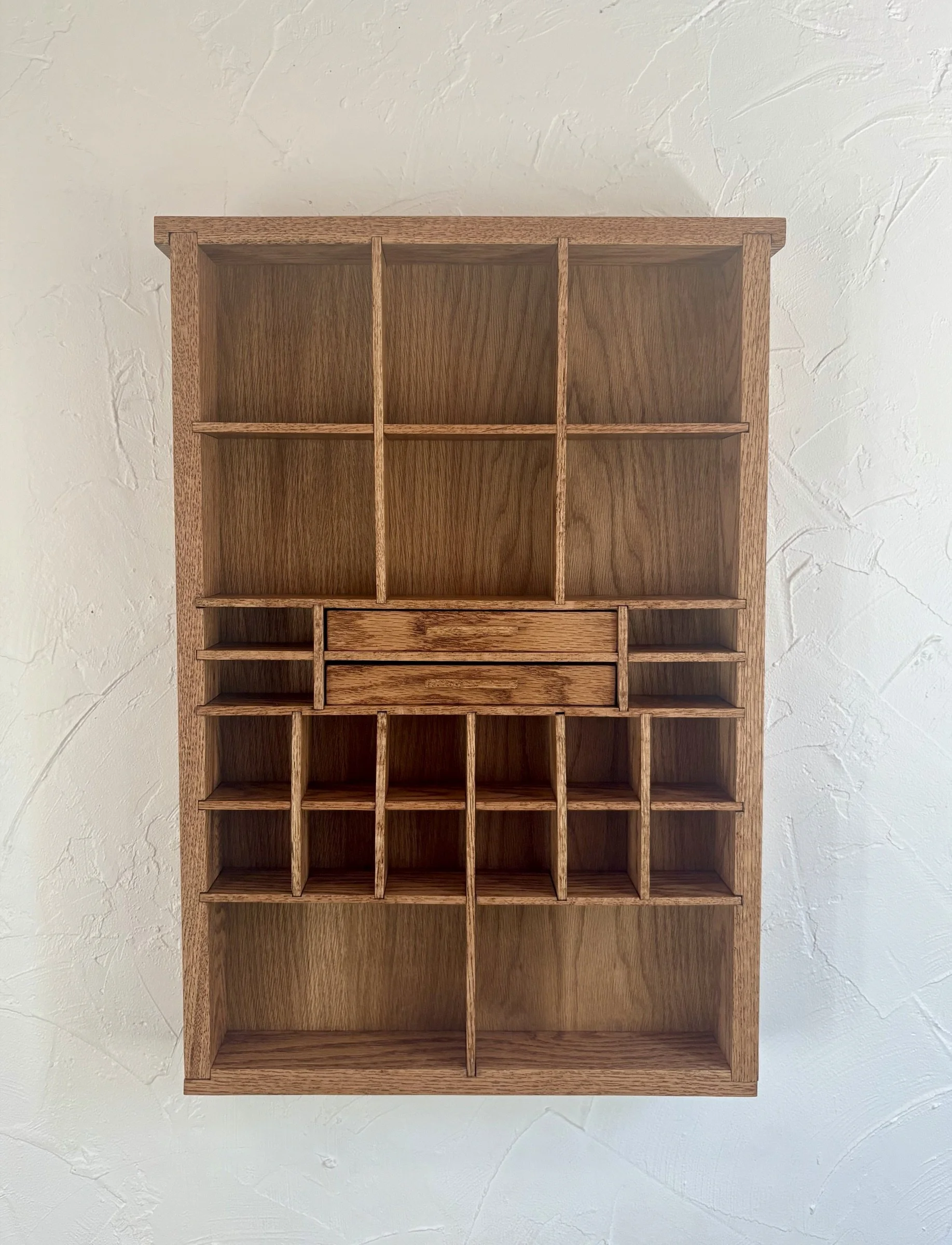 A wall-mounted oak curio shelf with compartments of varying size and a small center drawer.