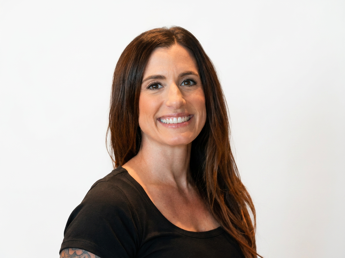 A smiling woman with long brown hair, wearing a black shirt, standing against a plain white background.