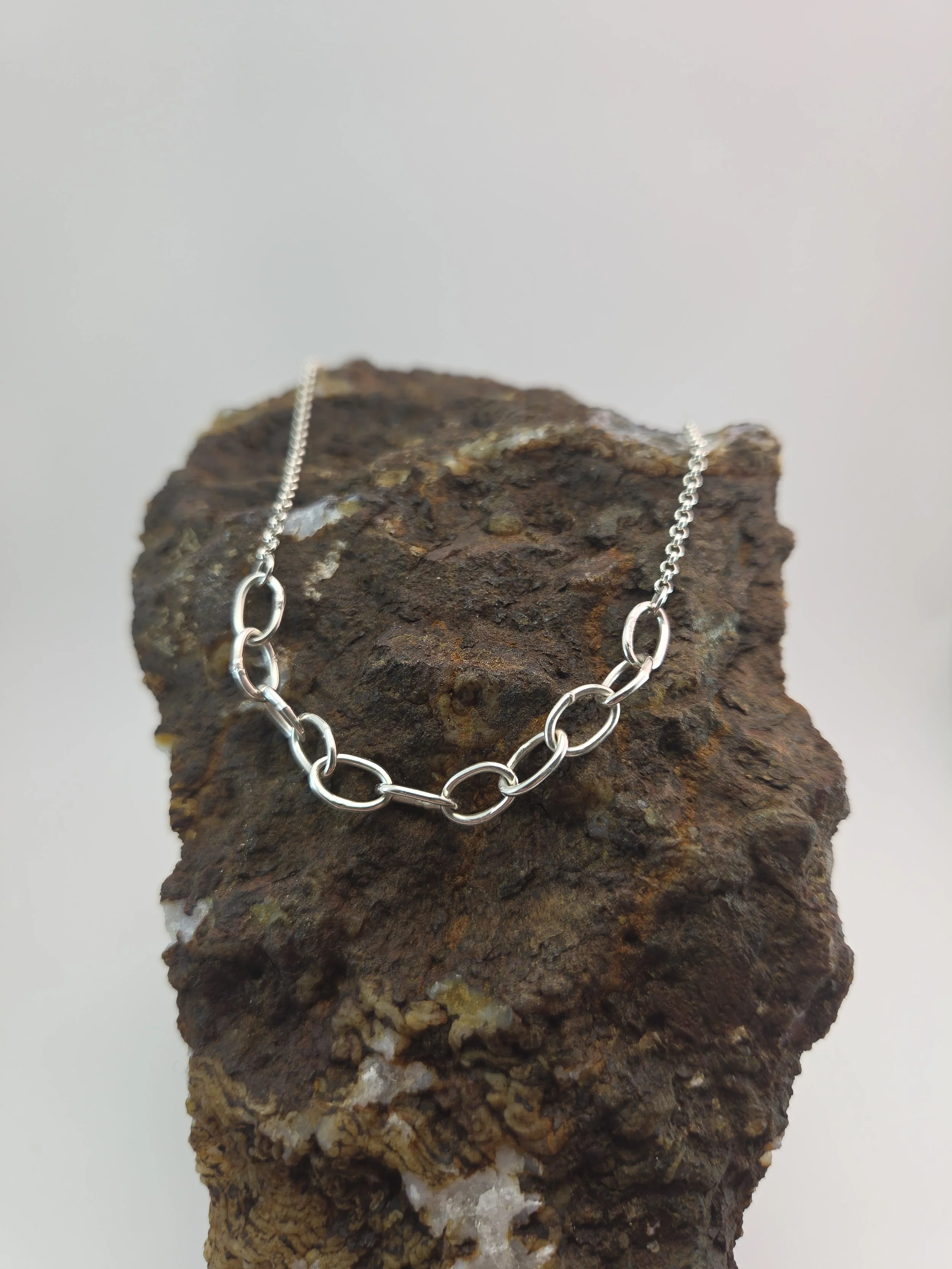 Silver chain necklace with small oval links displayed on a rough, textured rock