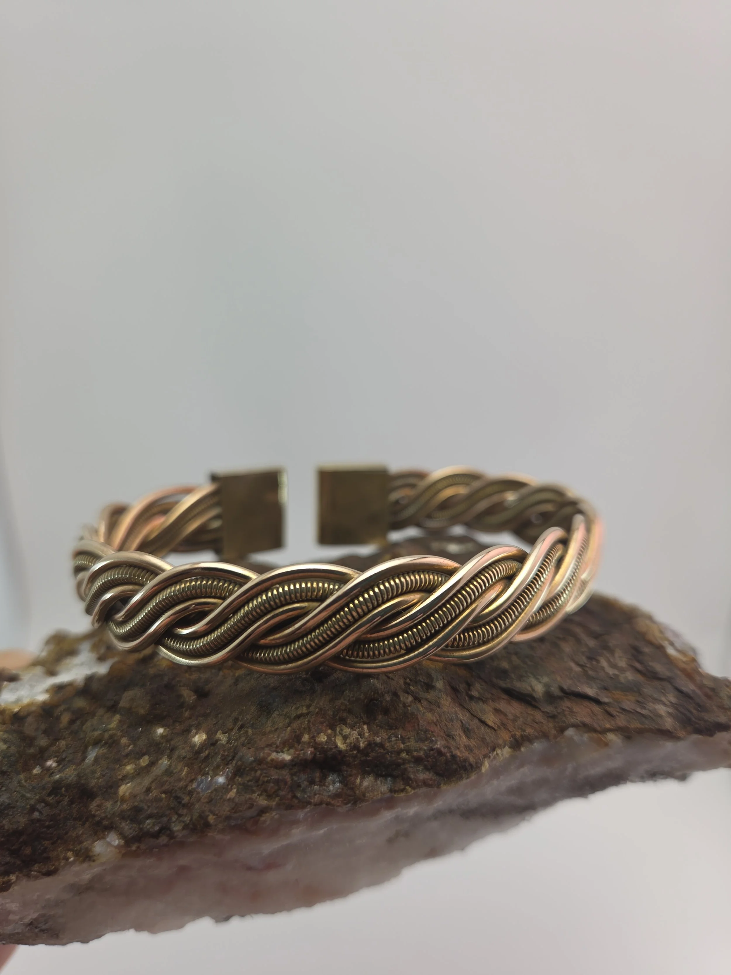 Close-up of a brass bracelet with intricate twisted design, resting on a rough, textured surface.