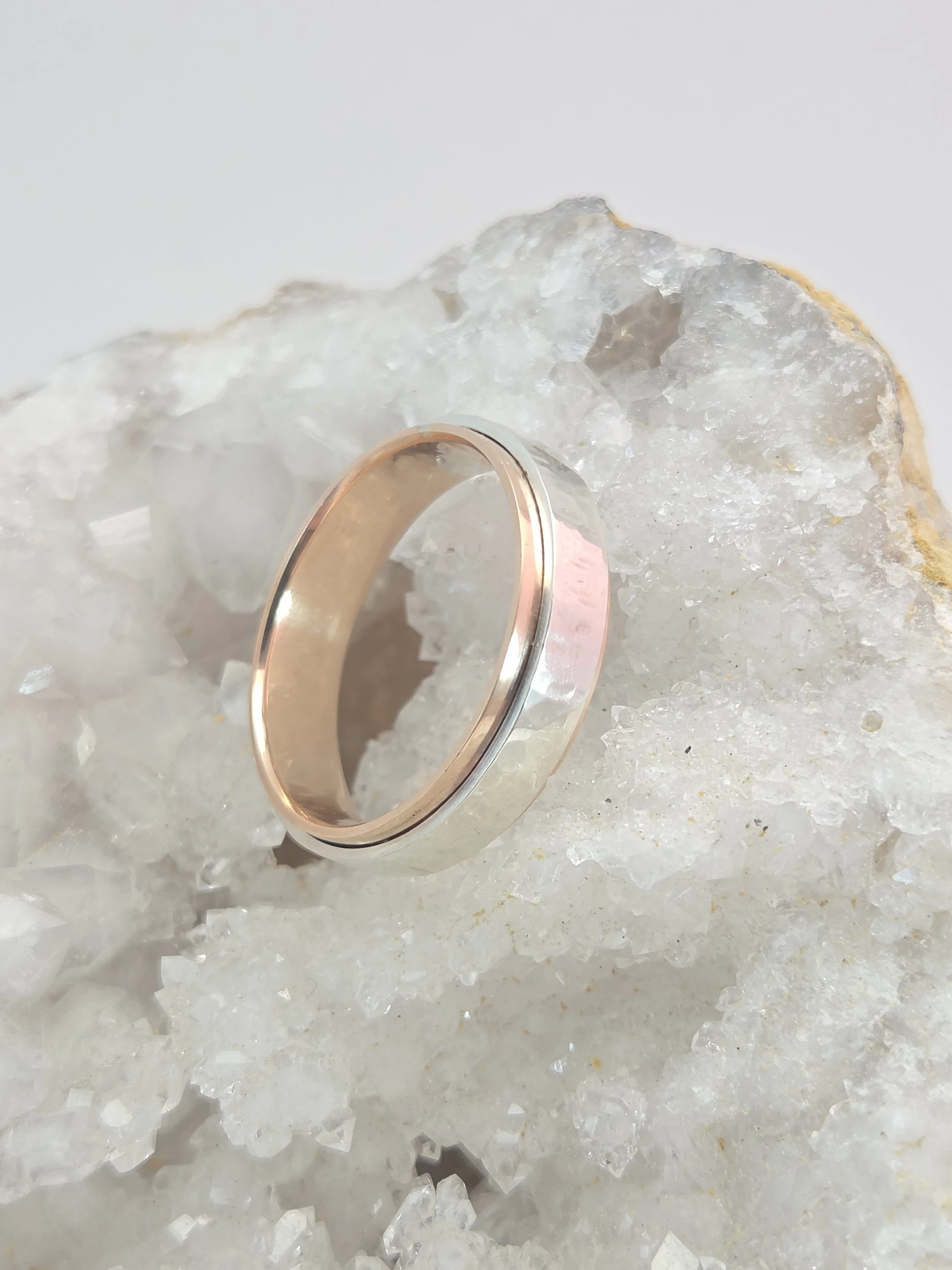A close-up image of two rings, one gold and one silver, placed on a bed of crystalline salt. The rings are shiny and reflecting light.