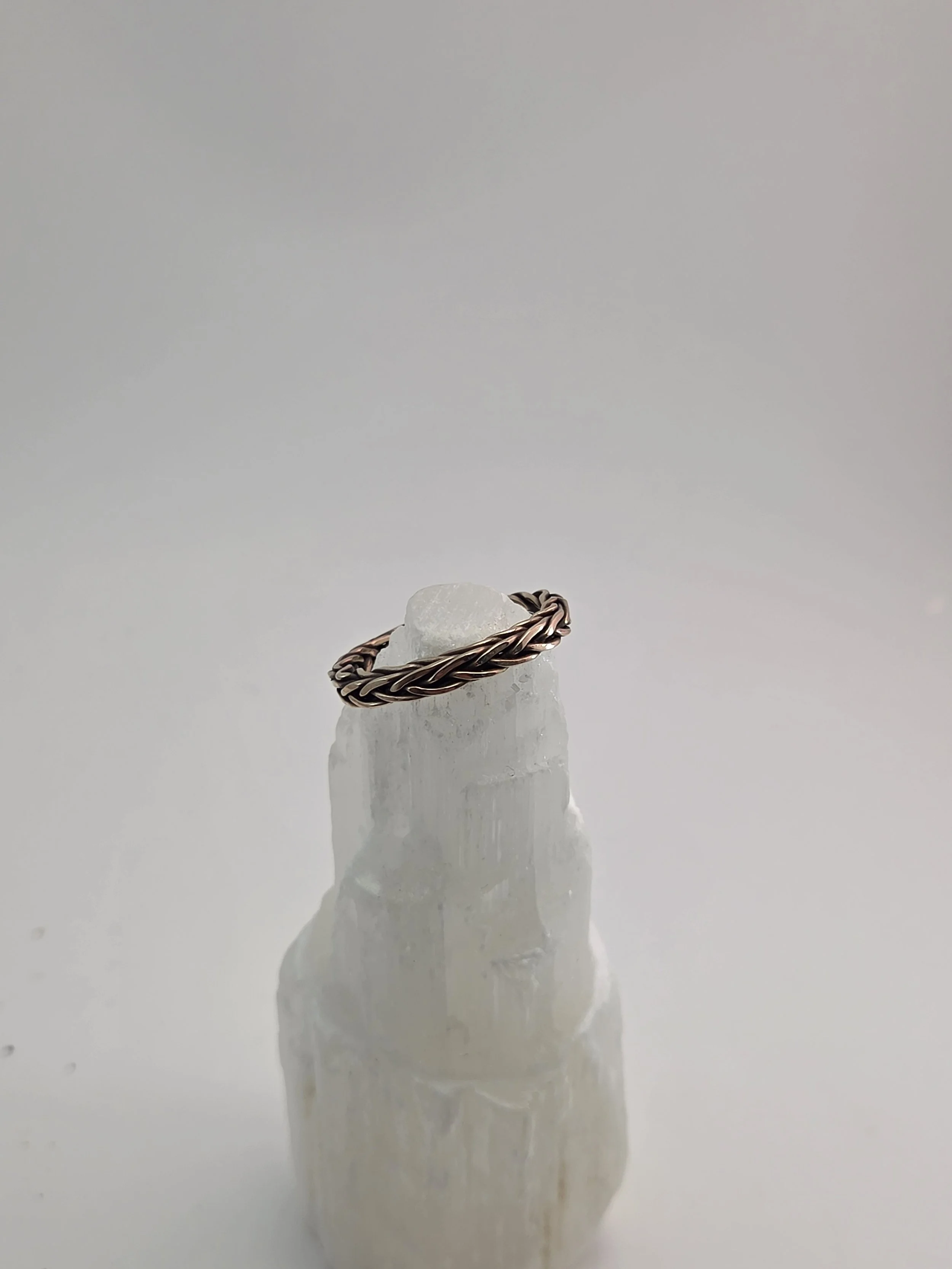 Bronze twisted ring placed on a piece of white mineral or crystal with a smooth, rounded top and rougher base, casting a shadow on a plain white surface.