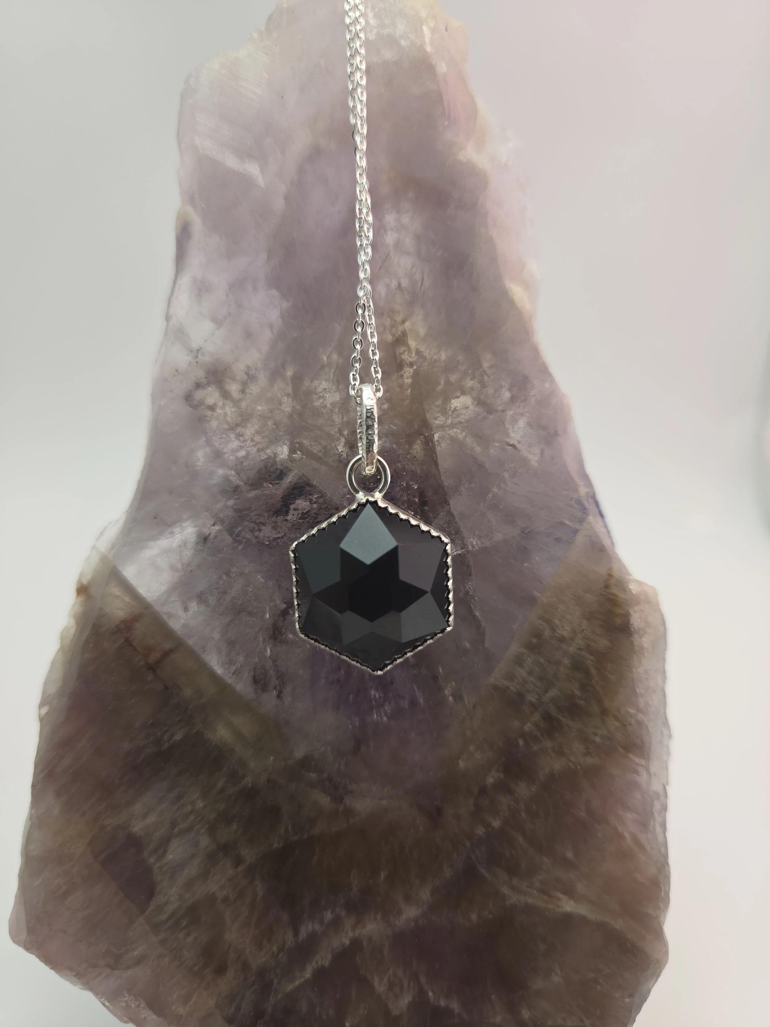 A necklace with a black hexagon-shaped pendant hanging from a silver chain, placed on a piece of polished mineral or stone.