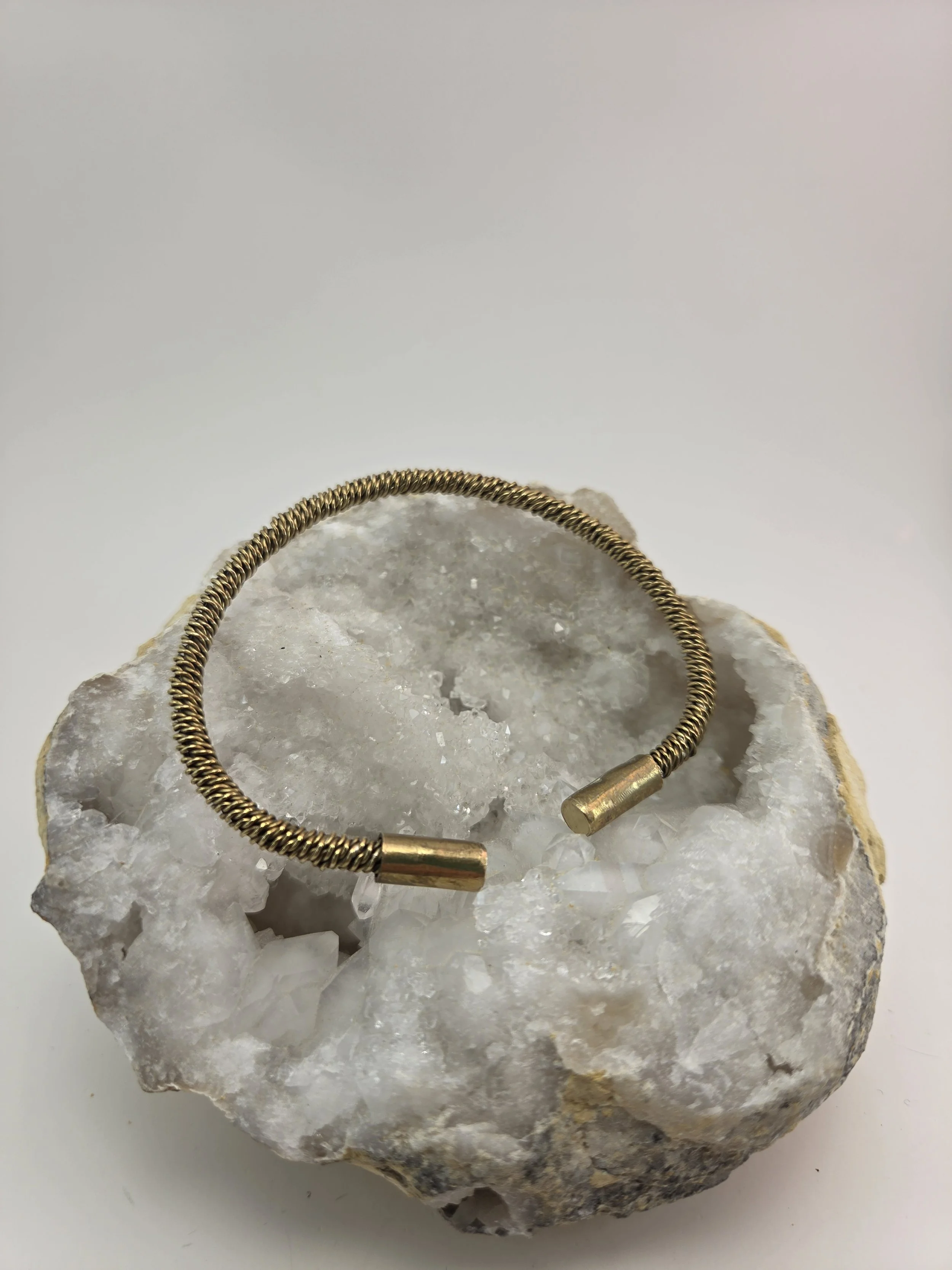 Brass bracelet with cylindrical ends, resting on a large mineral or rock with a rough, crystalline surface.