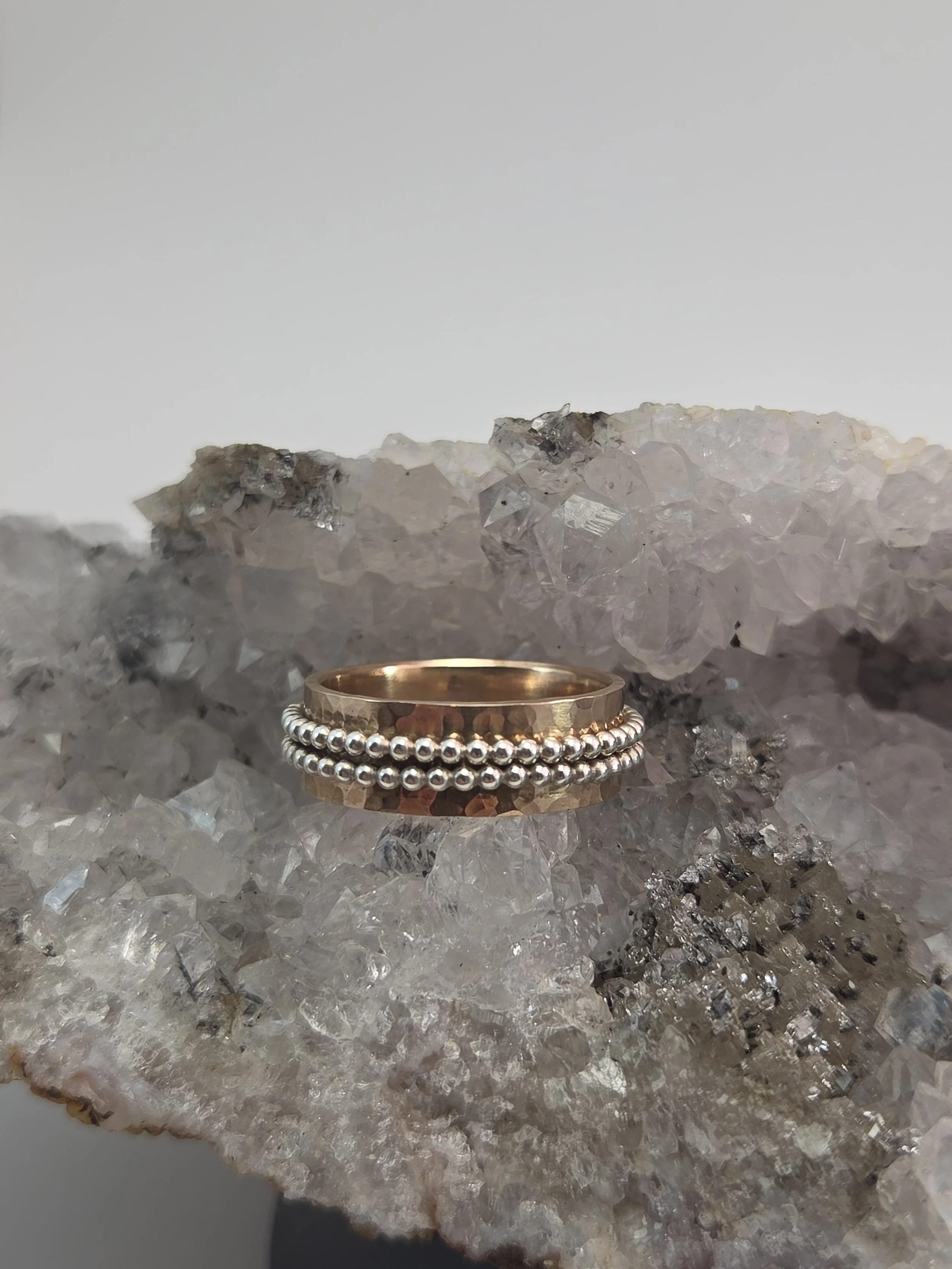 A bronze ring with small silver beads around it placed on a rock with a rough, crystalline texture.
