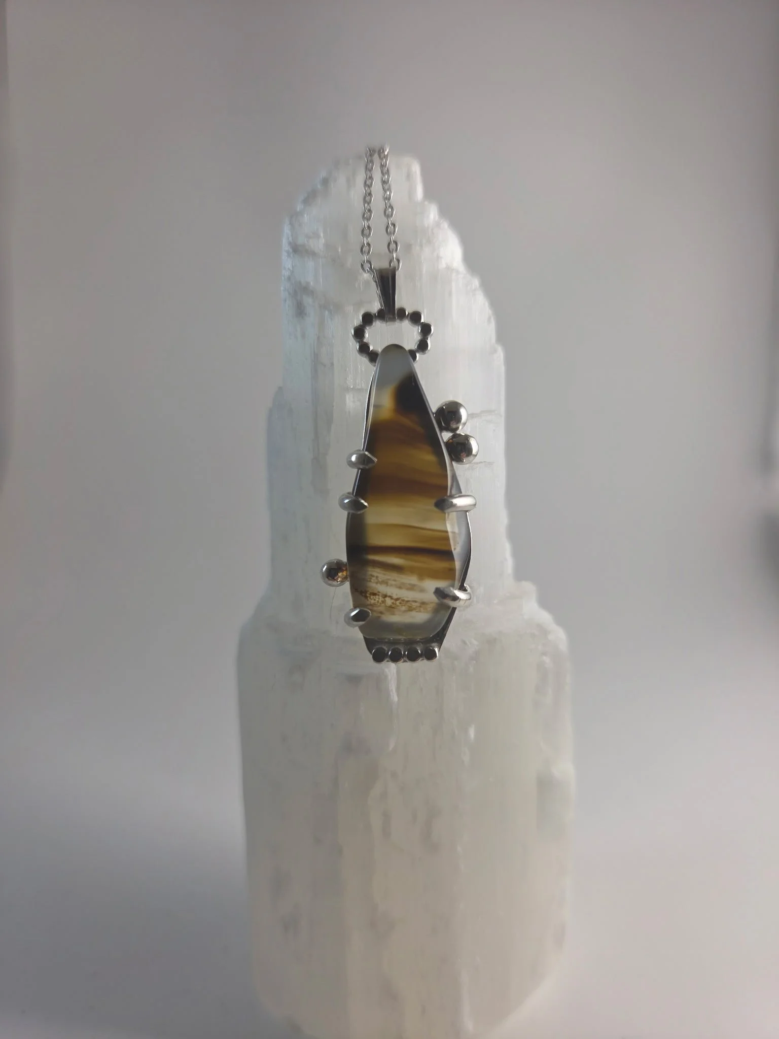 A necklace with a unique-shaped pendant featuring brown, black, and ivory-colored bands, hanging from a silver plated chain.