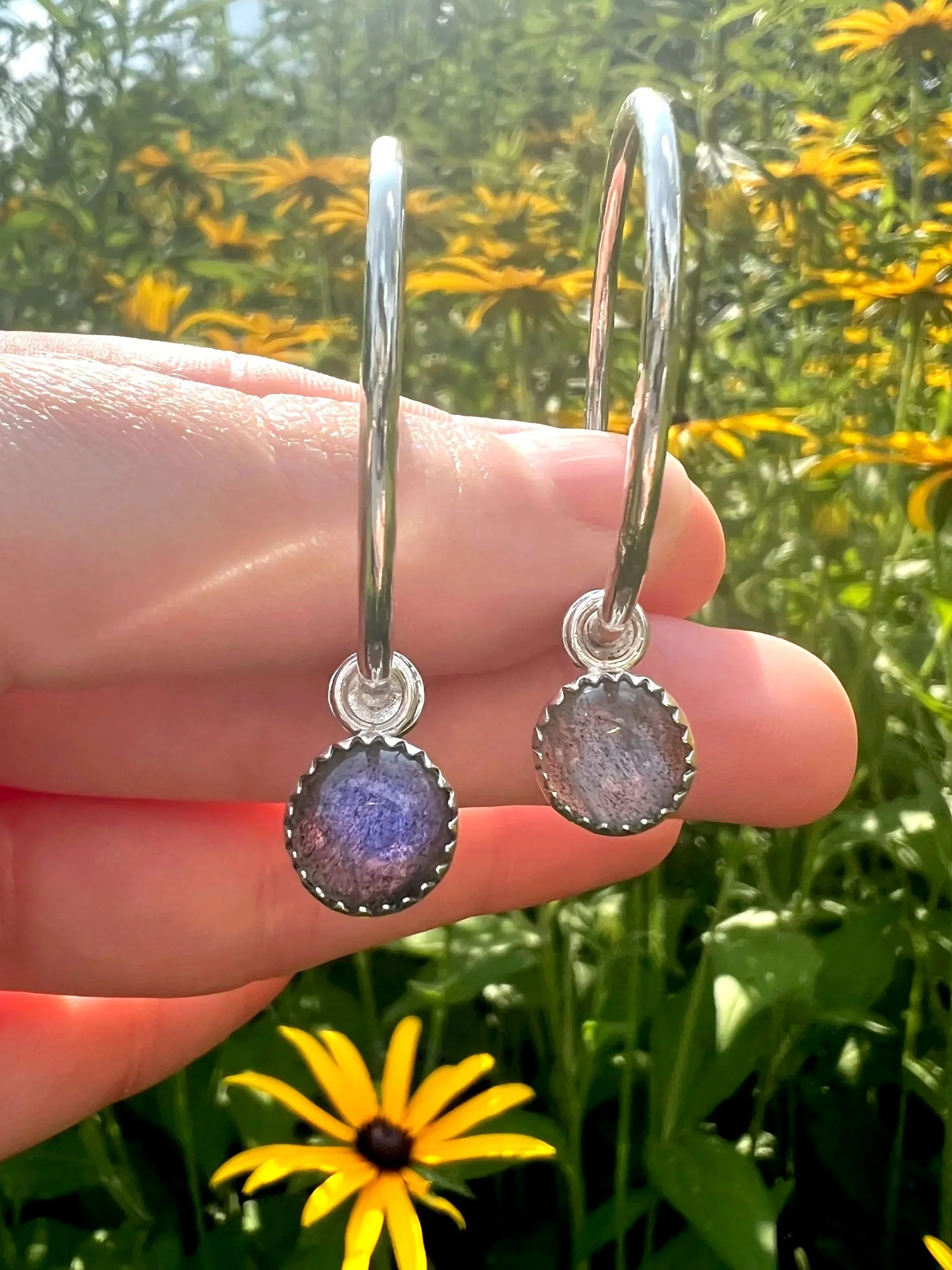 silver hoop earrings with labradorite charms in front of yellow flowers