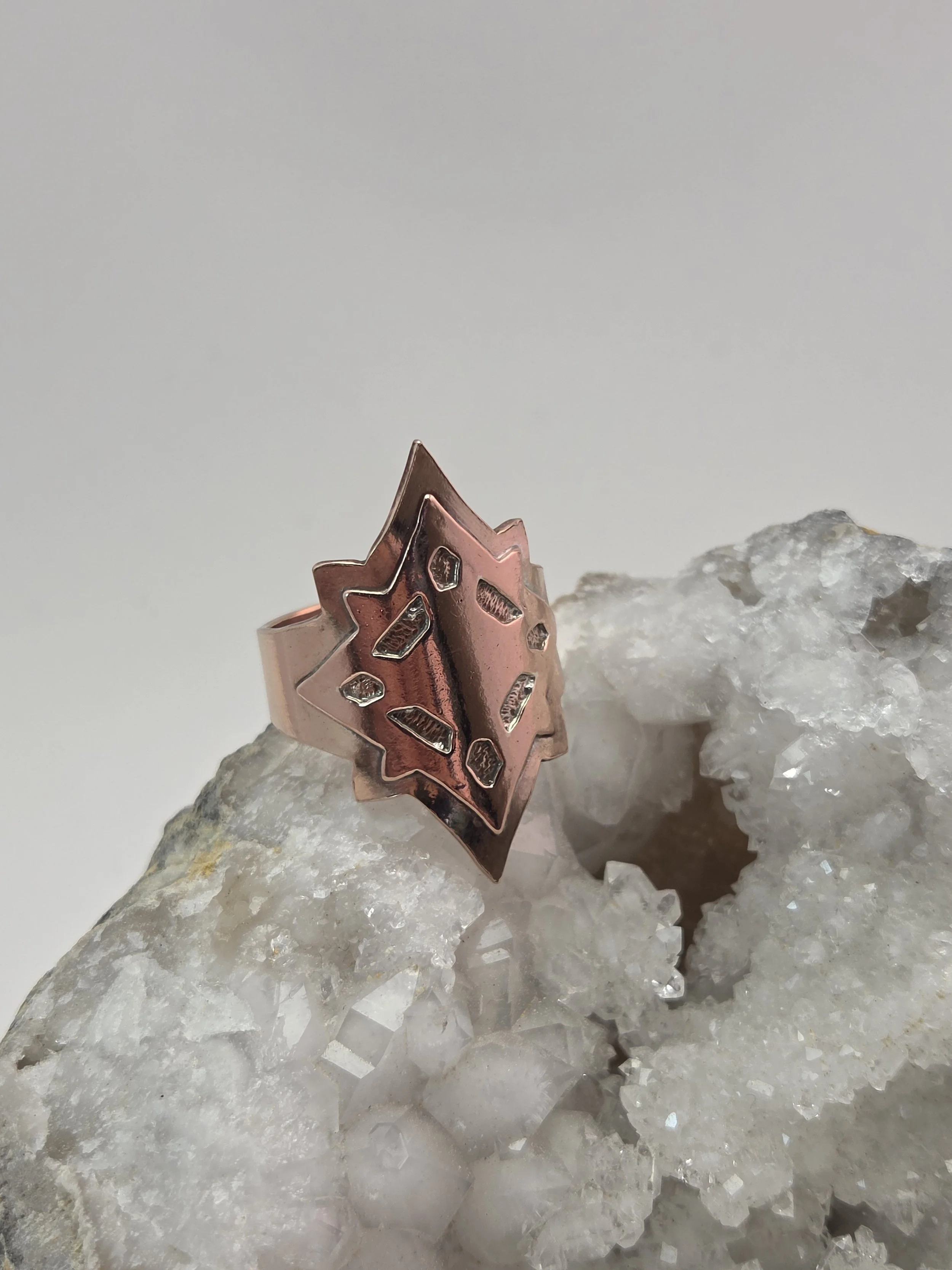 Close-up of a bronze and copper star-shaped ring with cutout patterns, resting on a large cluster of white quartz crystals.