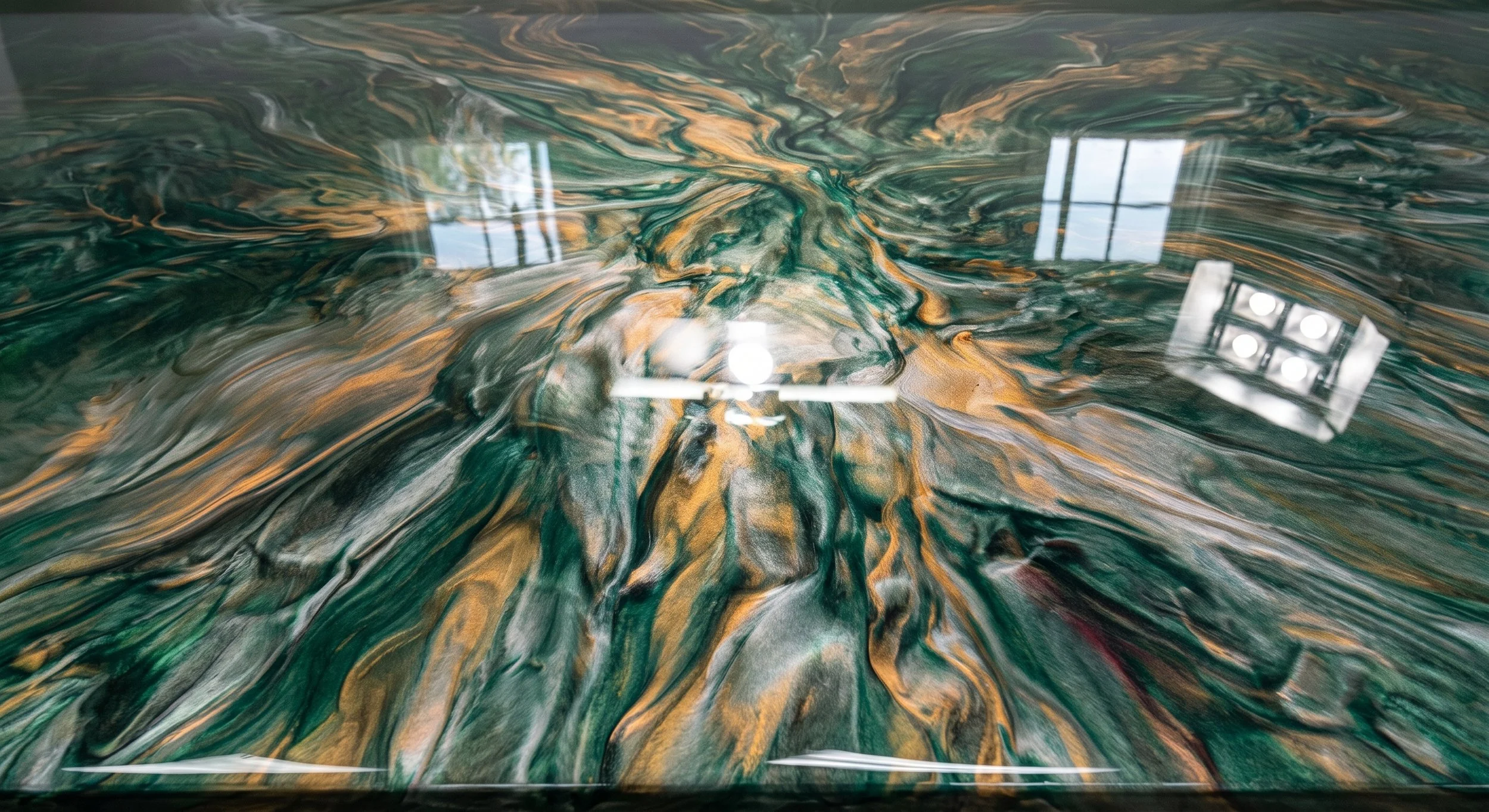 Close-up photo of a swirling, multicolored marble surface with a glossy finish, reflecting overhead lights and window panes.