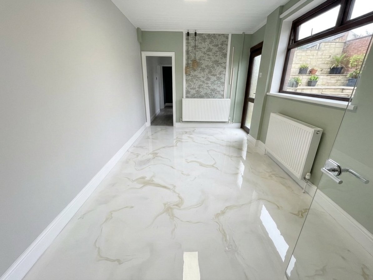 Empty room with white marble floor, light green walls, large windows with a view of outdoor plants, radiator, and a door leading to a hallway.