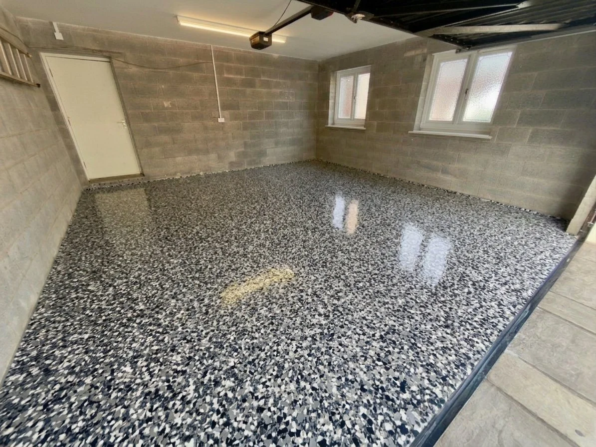 Empty garage with exposed brick walls, two windows, a closed door, and a polished terrazzo floor.