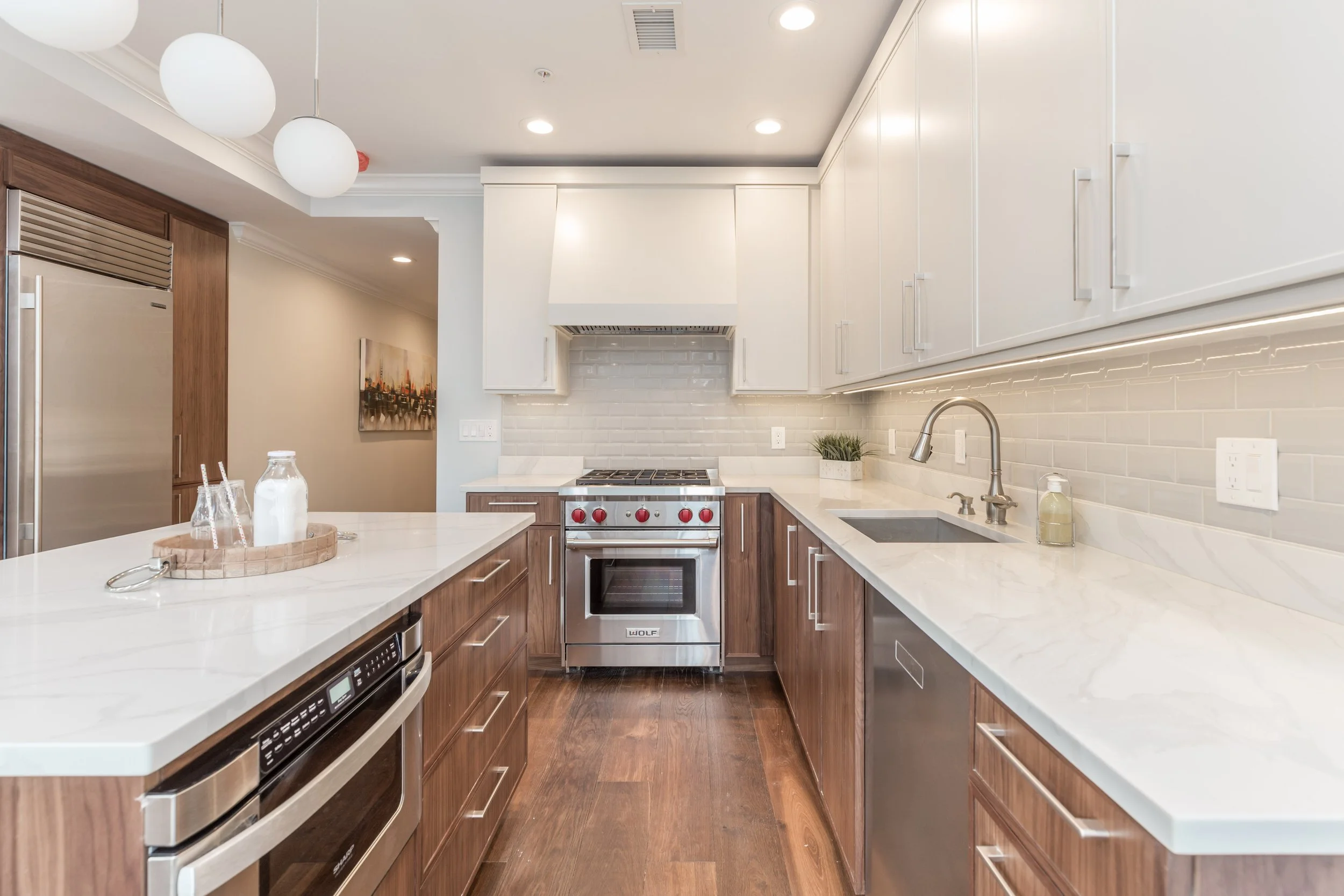 Modern kitchen with white countertops, wood cabinets, stainless steel appliances, white subway tile backsplash, and a small plant near the sink.