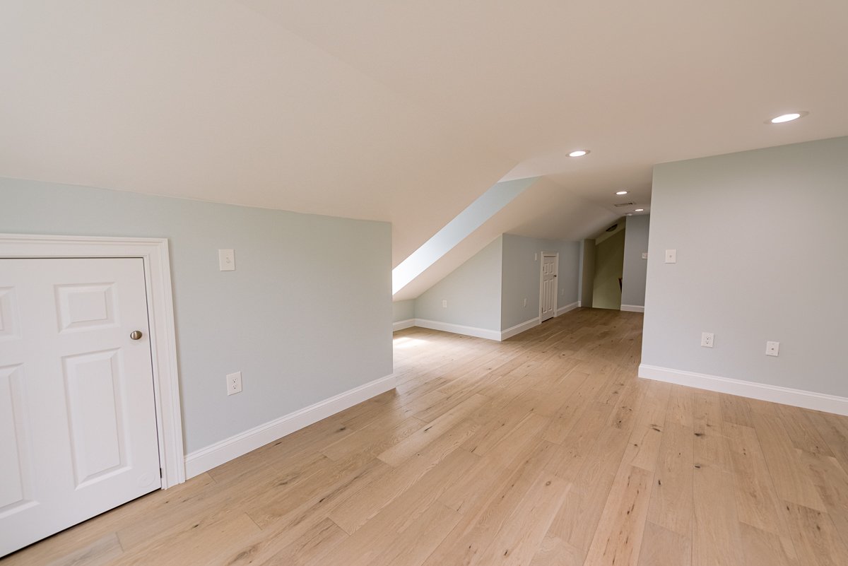 Empty attic room with sloped ceiling, wooden floors, and white walls, featuring small doors for storage.