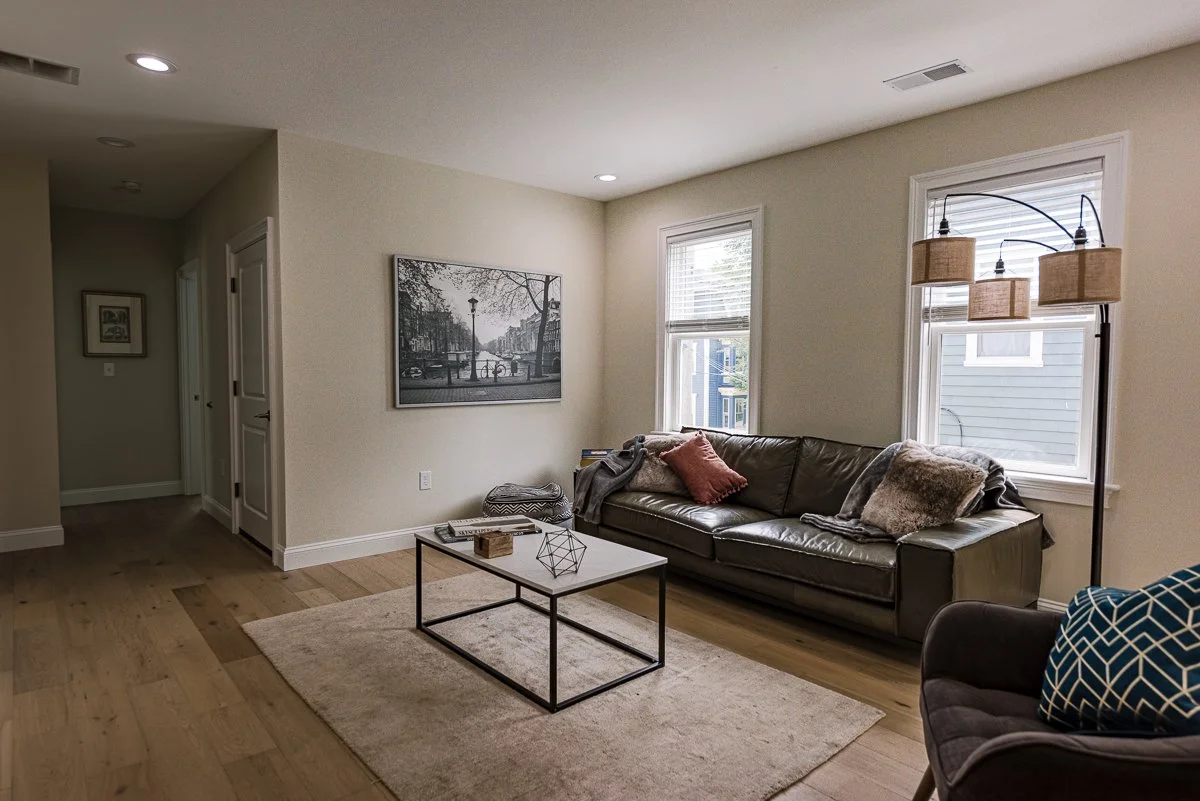 Living room with a black leather sofa, window blinds, a coffee table, and a floor lamp with three woven lampshades.