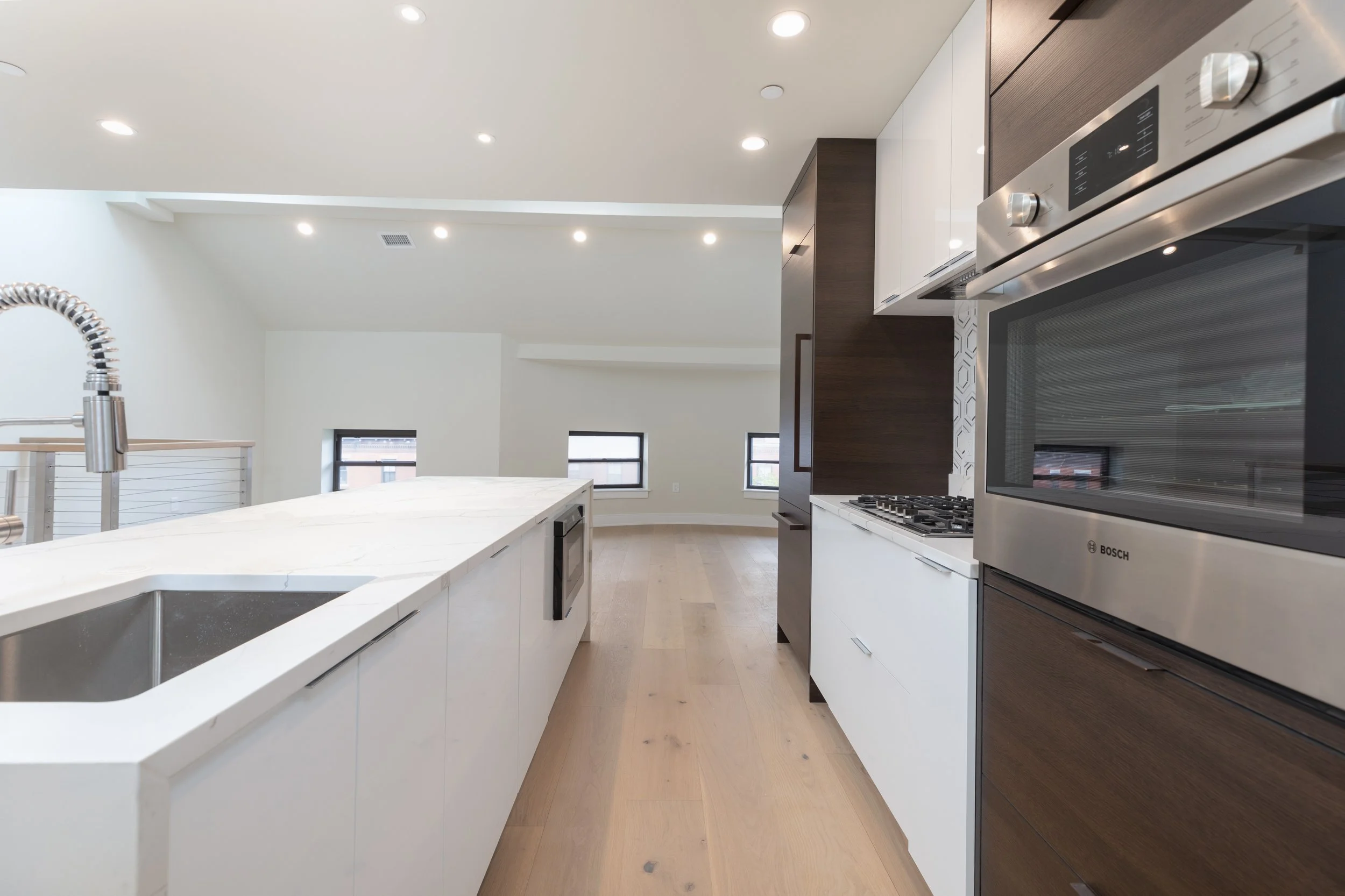 Modern kitchen with white island, stainless steel sink, dark wood and white cabinets, stainless steel oven, and hardwood flooring.