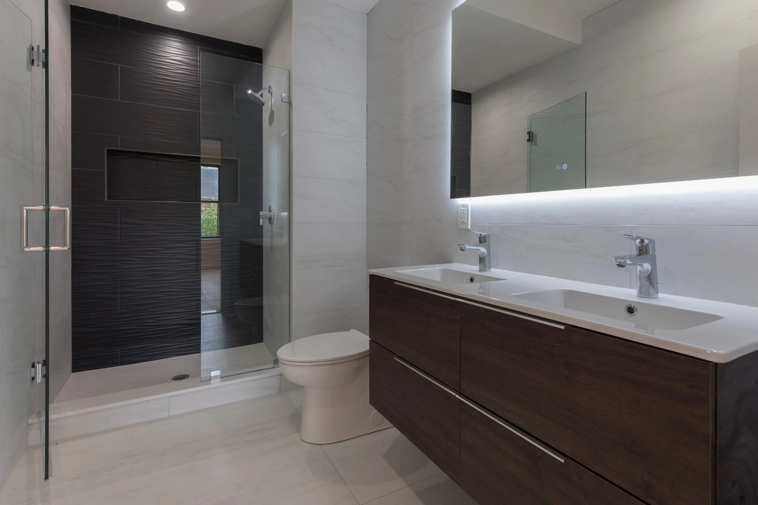 Modern bathroom with double sink vanity, large mirror, and walk-in shower with glass door.