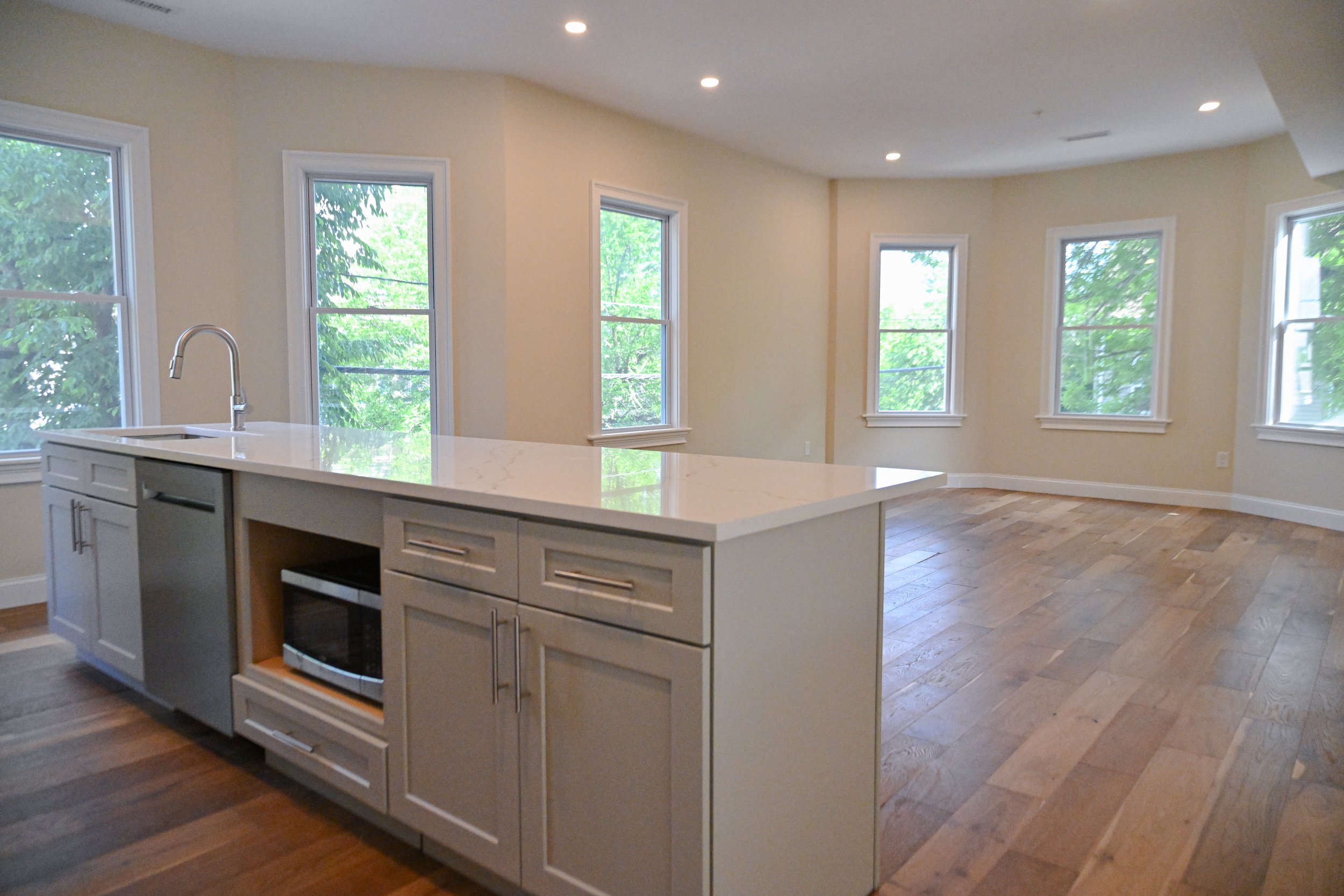 Open-concept kitchen with white island, six windows letting in natural light, wooden flooring, and neutral-colored walls.