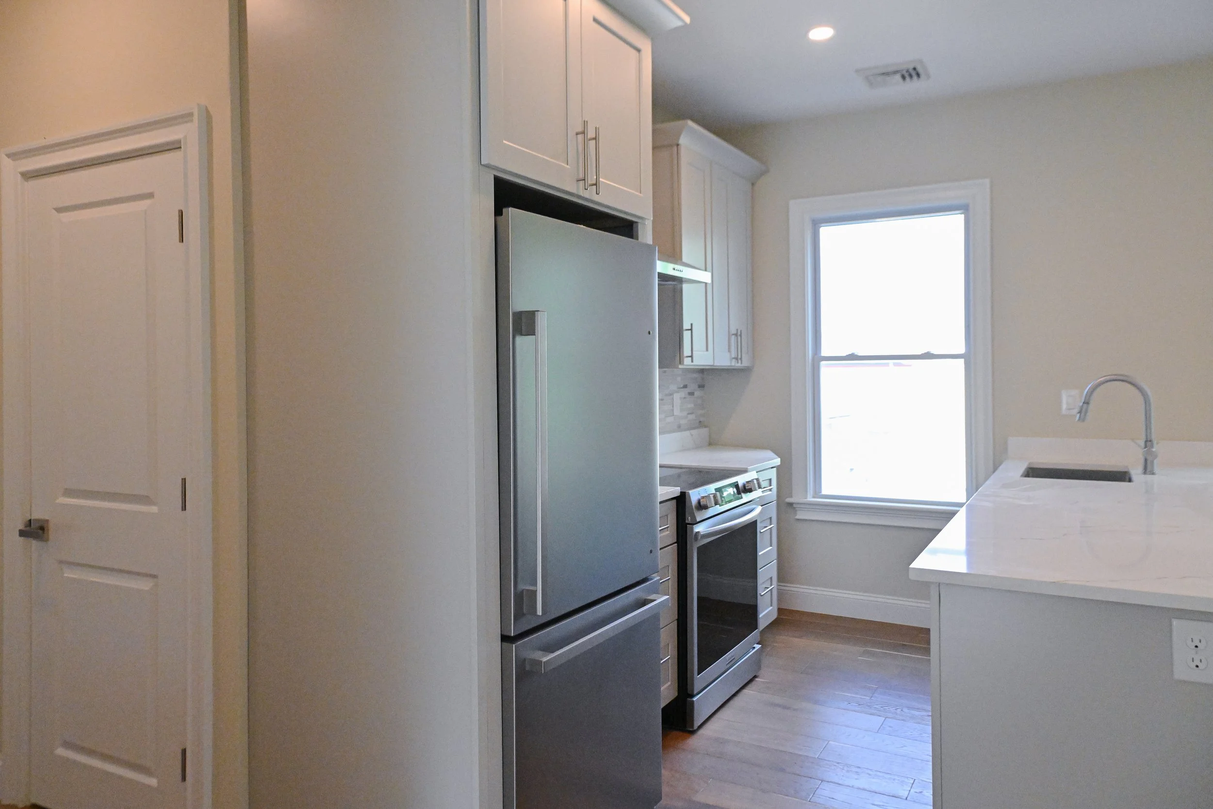 Kitchen with white cabinets, stainless steel oven, refrigerator, and a window above the sink in natural light.