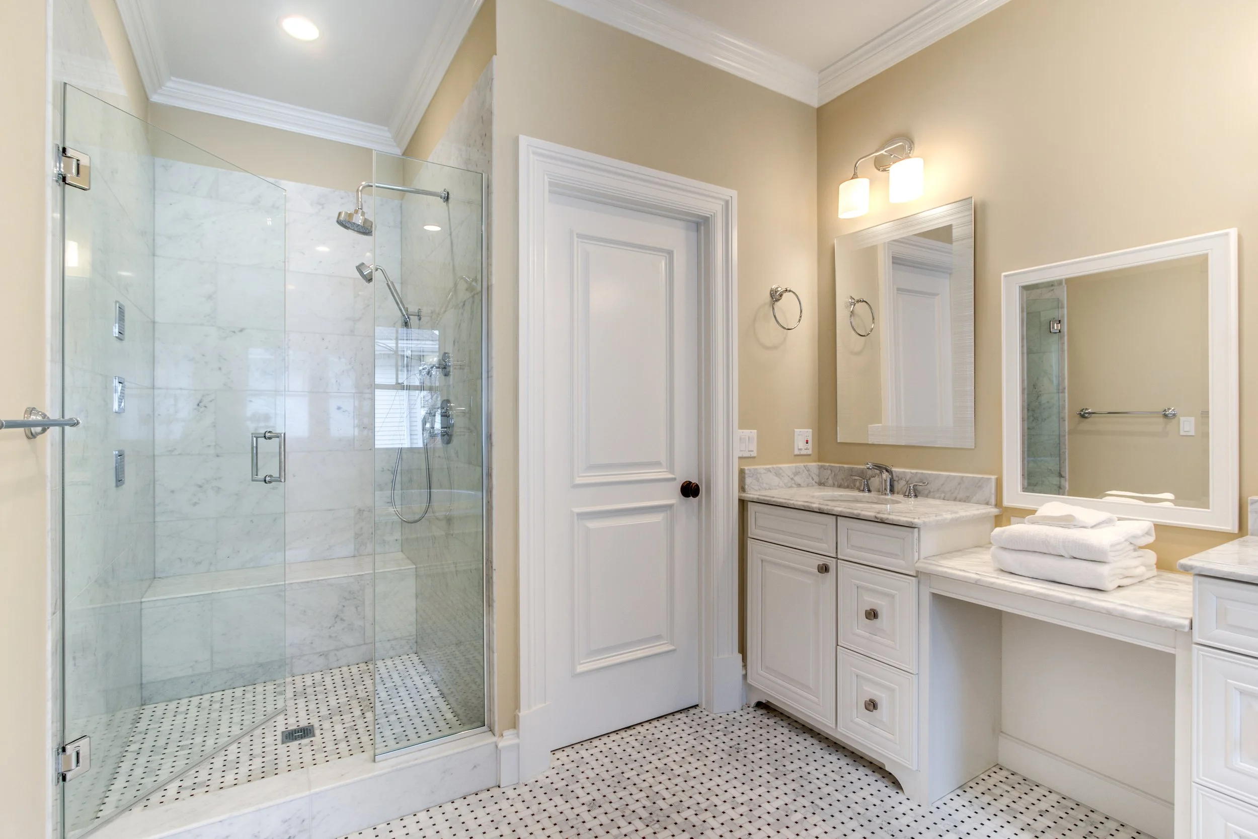 Bathroom with a glass-enclosed shower, a white vanity with a marble countertop, a mirror, and beige walls.