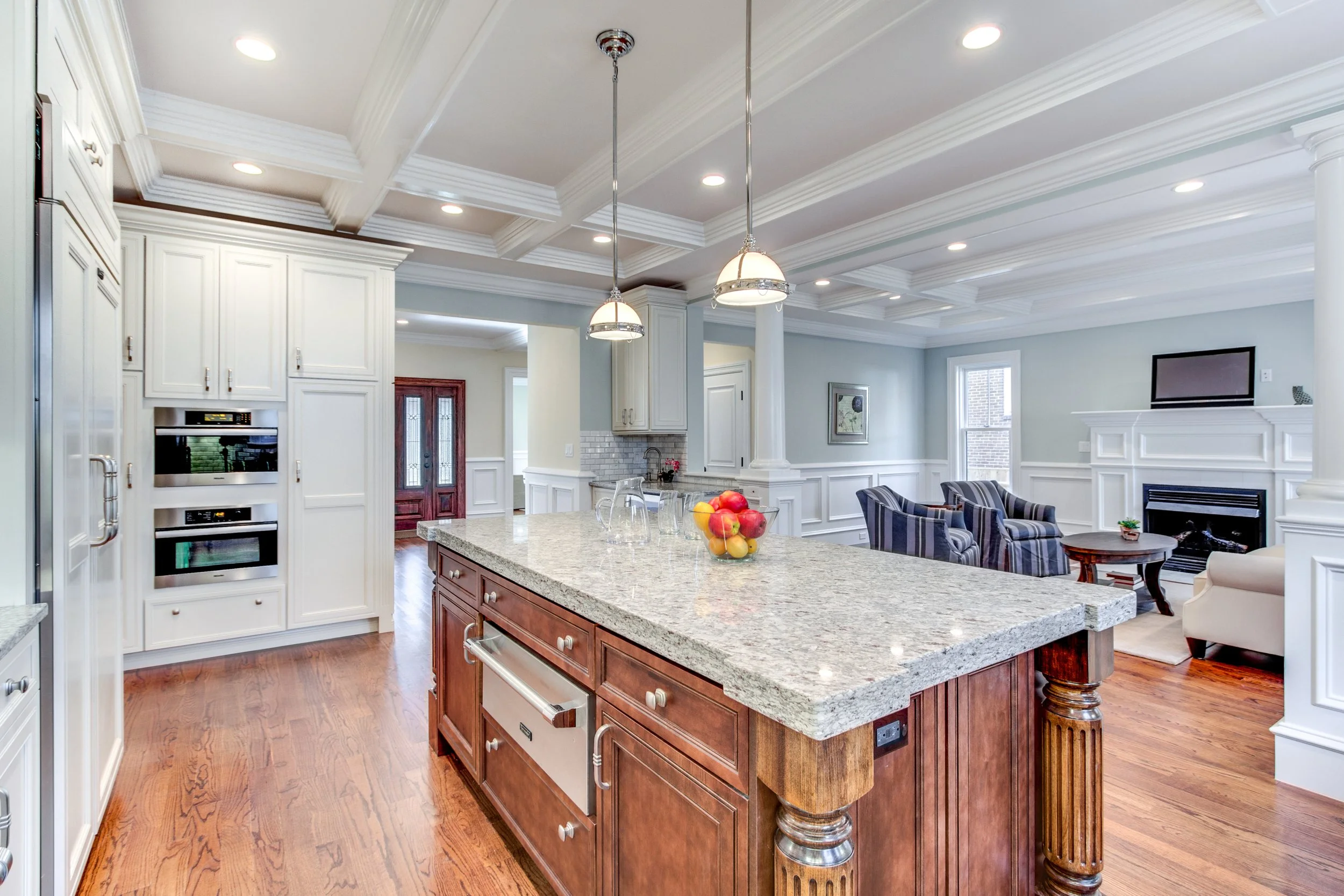 Open-concept kitchen and living room with a granite island, white cabinets, a fireplace, and a sitting area with striped chairs.