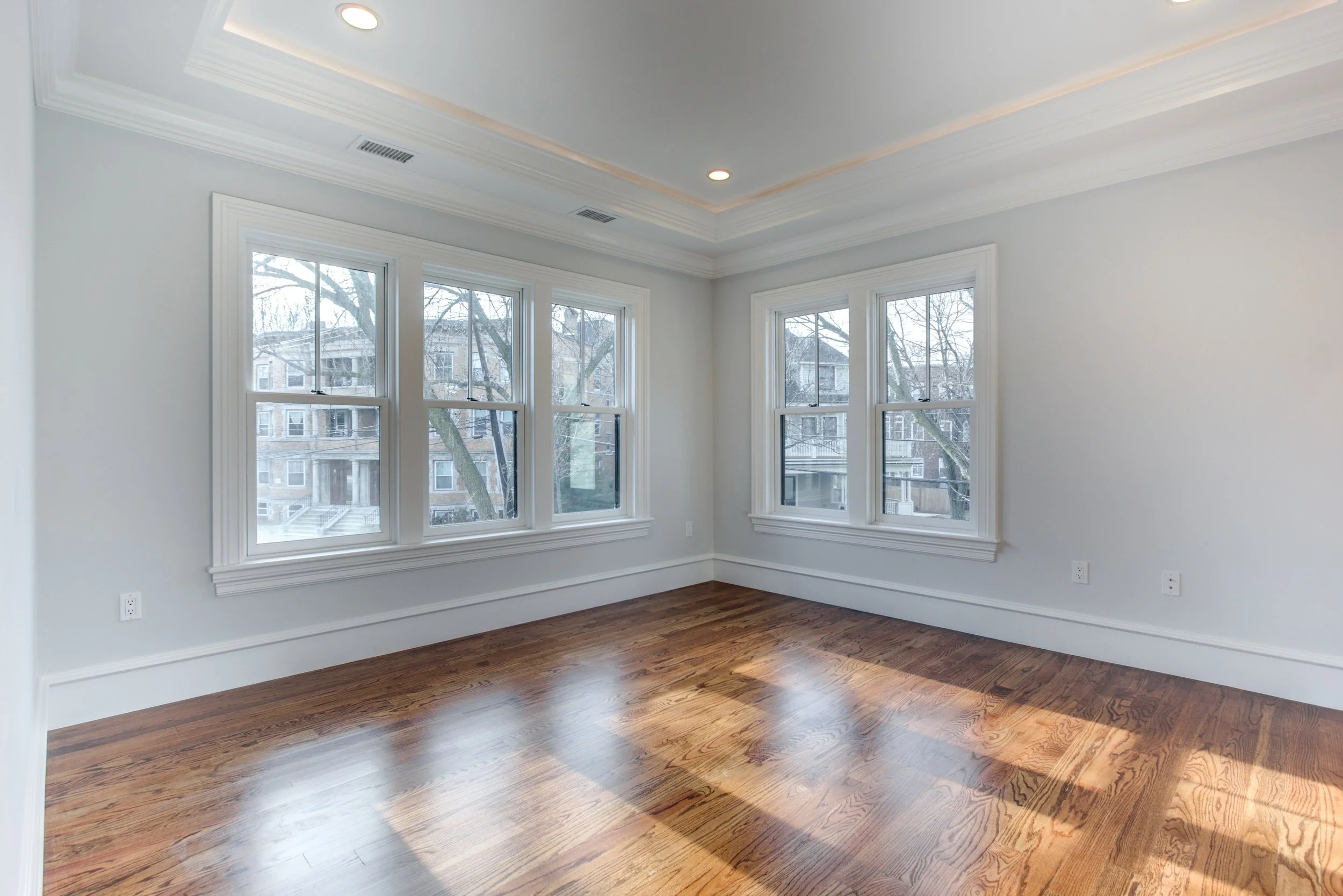 Empty room with hardwood floors, white walls, large windows, and ceiling lighting.