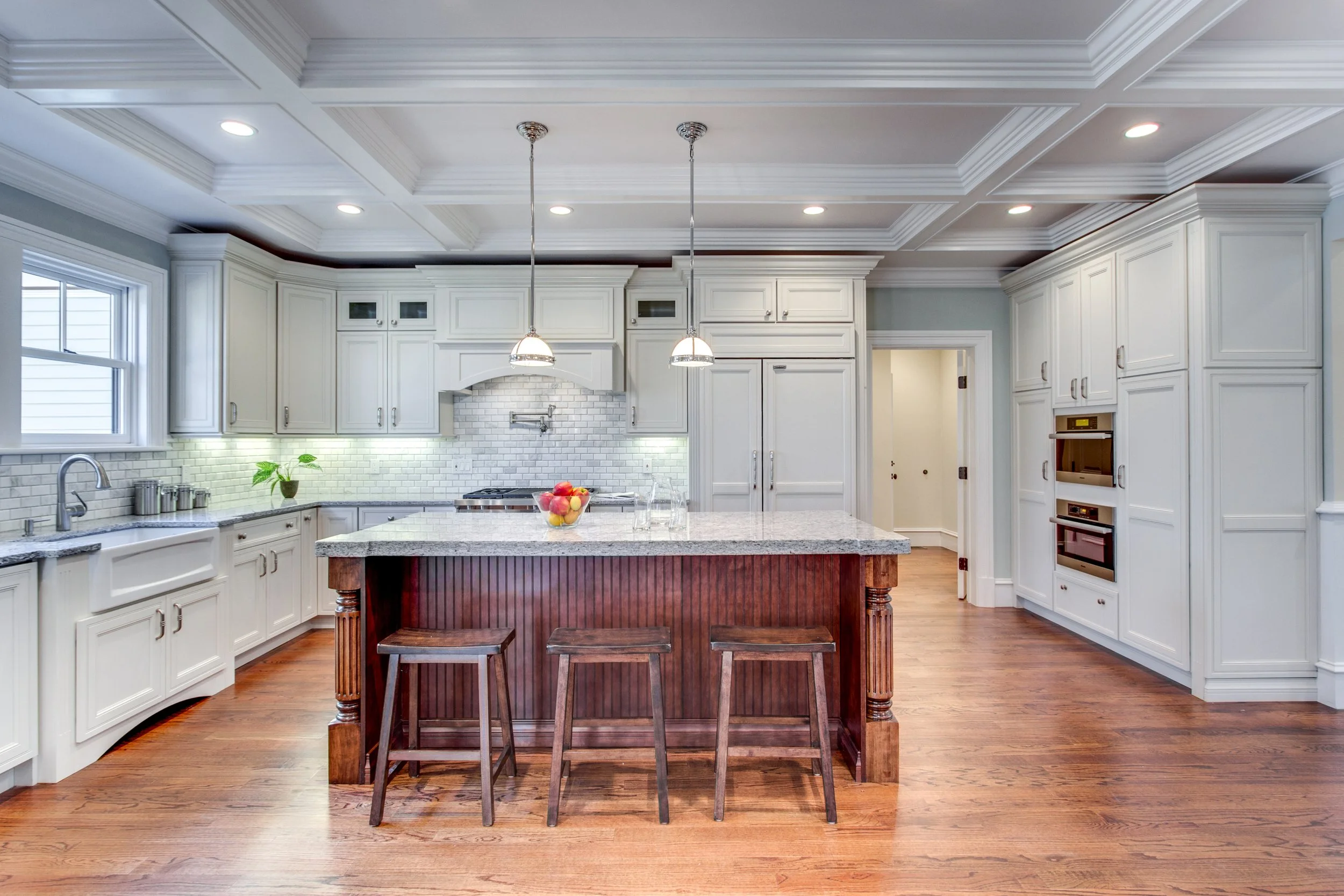 Modern white kitchen with granite countertops, a central island, a bowl of apples, pendant lighting, cabinetry, and hardwood floors.