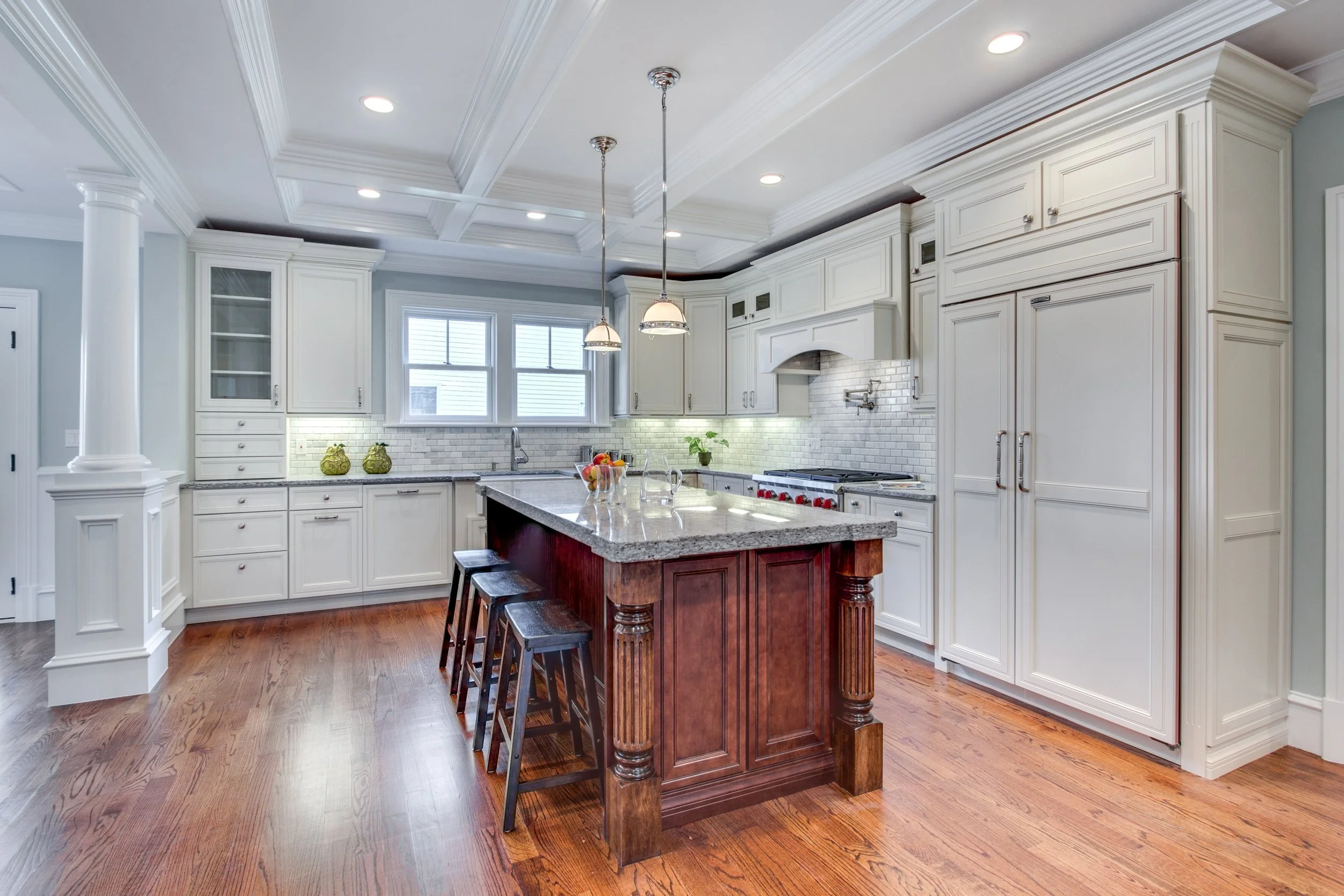 Kitchen with white cabinets, a gray granite island, pendant and recessed lighting, a white brick backsplash, and hardwood floors.