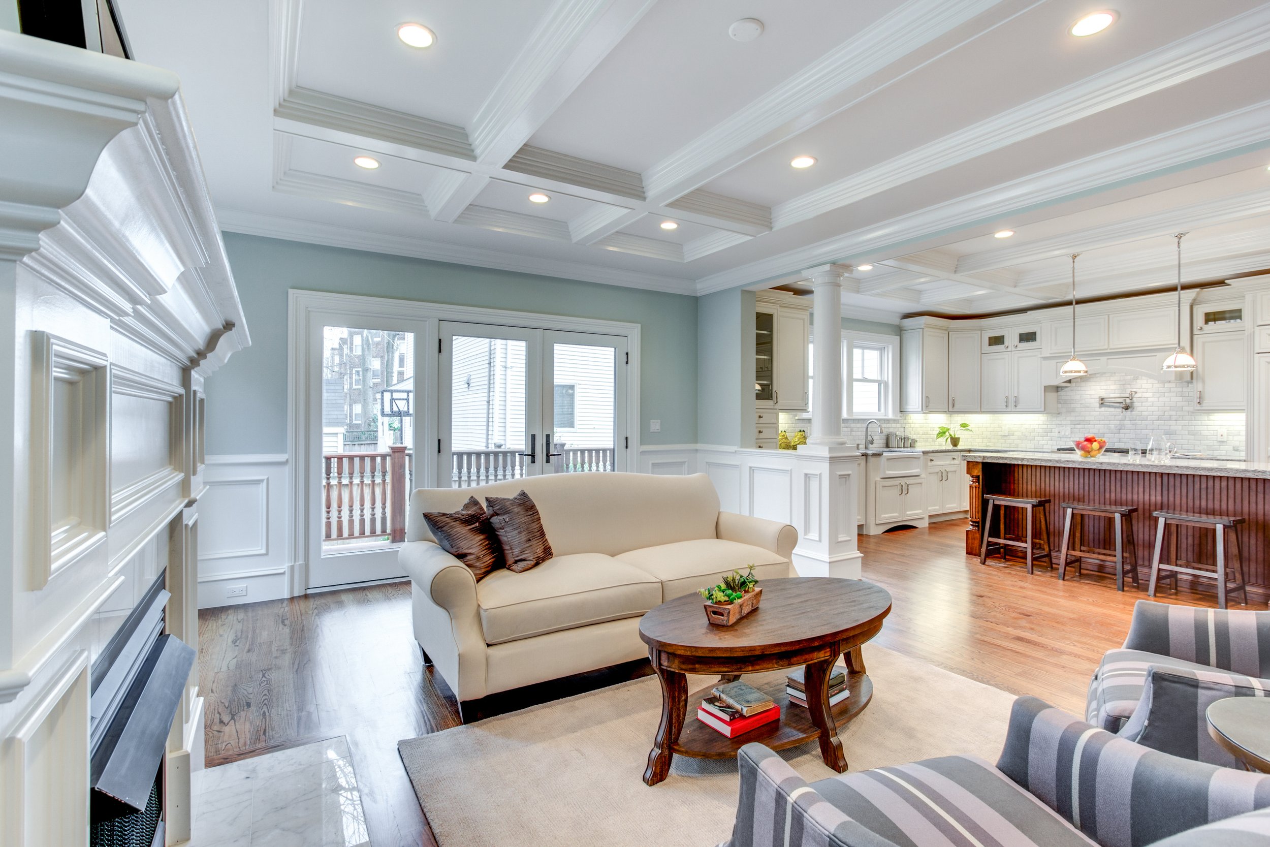 Open-concept living room and kitchen with white cabinetry, hardwood floors, and a coffered ceiling with recessed lighting.