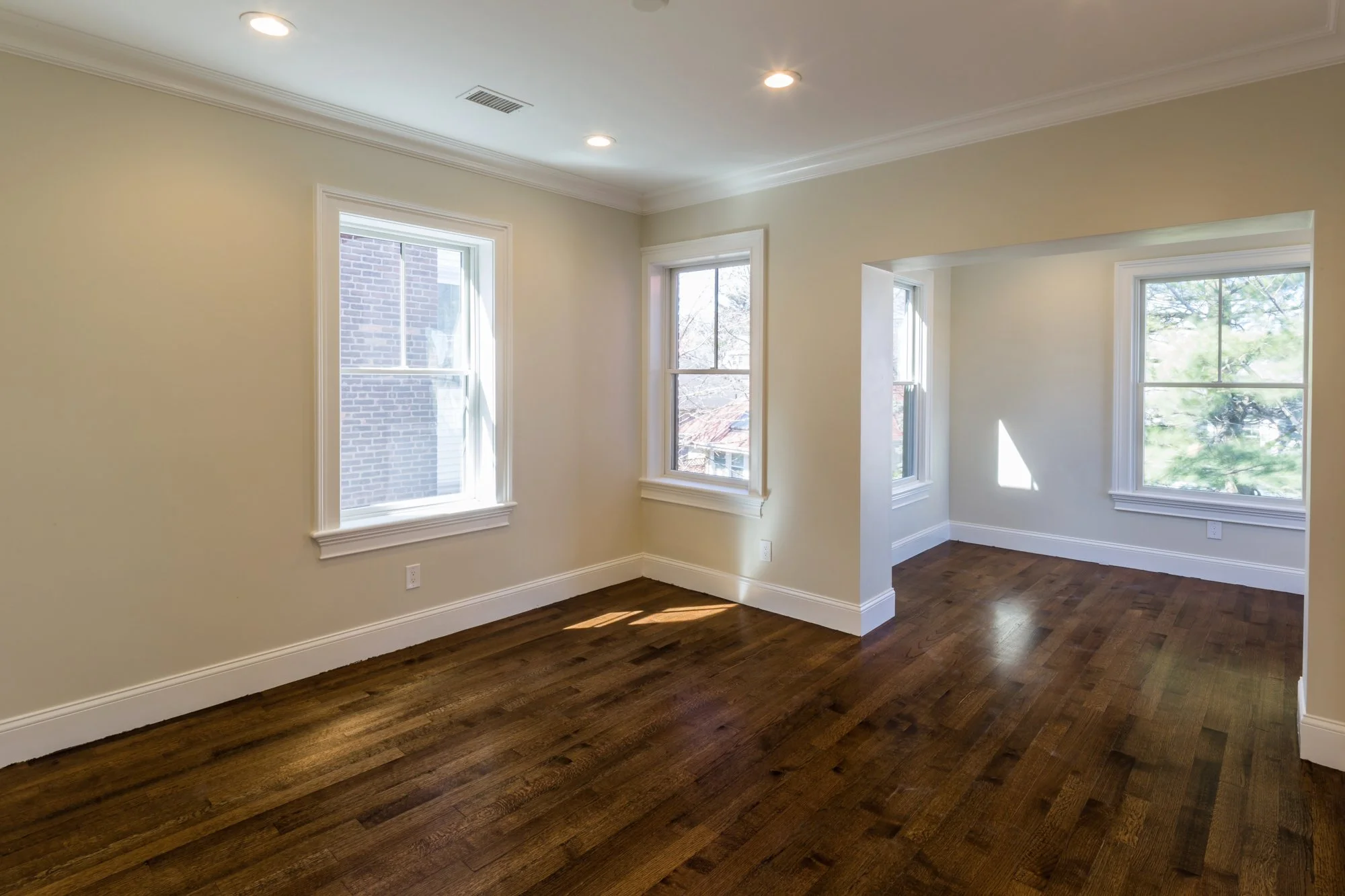 Empty room with white walls, crown molding, hardwood flooring, and large windows allowing natural light.