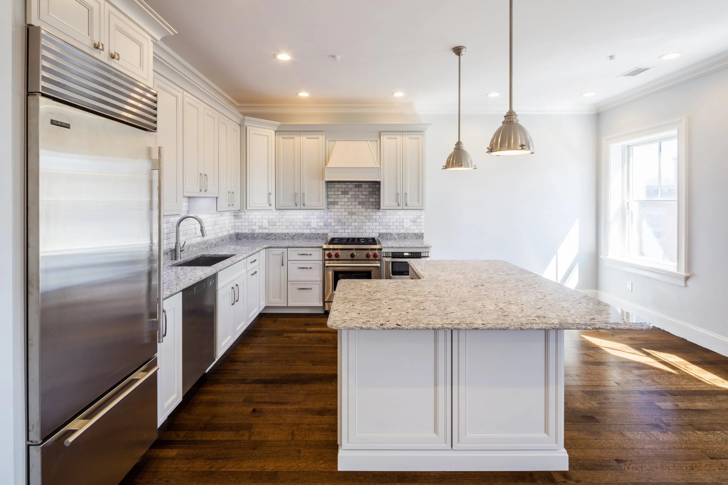 Modern kitchen with white cabinets, granite countertops, stainless steel appliances, pendant lighting, and hardwood floors.